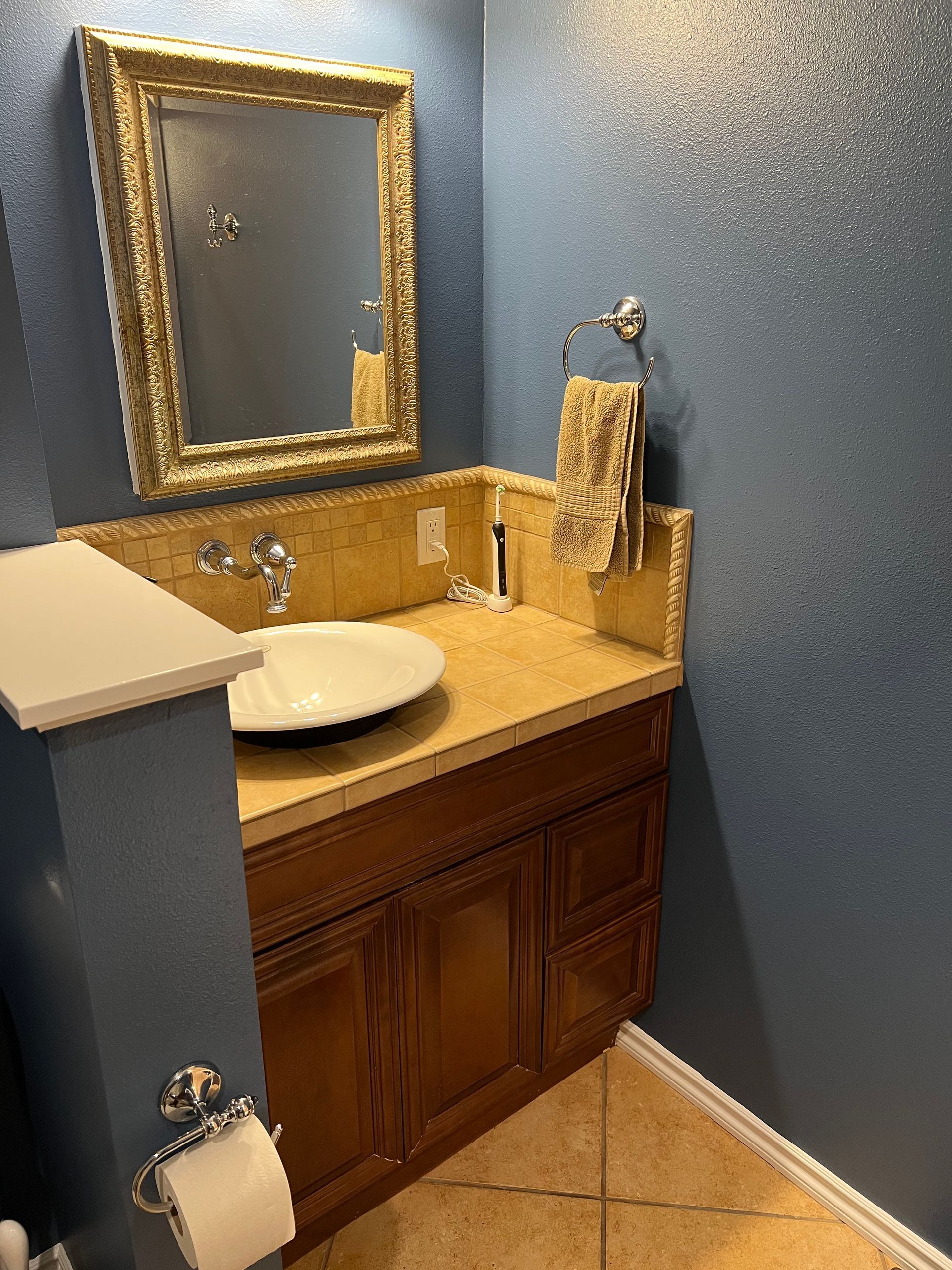 Small bathroom vanity with gold-framed mirror, white sink, tan countertop, and blue walls.