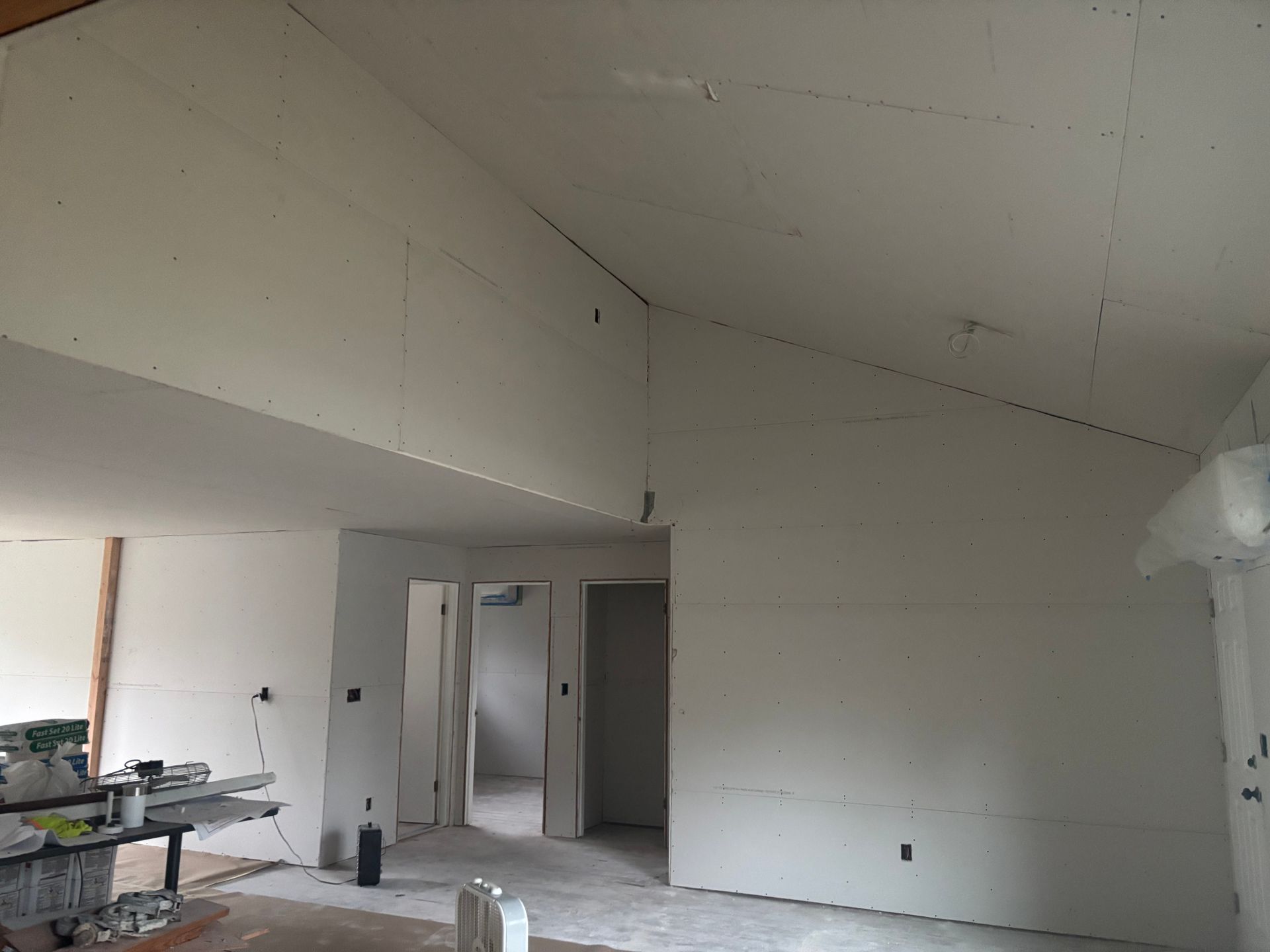 Empty white room under construction with exposed ceiling, unfinished walls, and construction materials on the left.