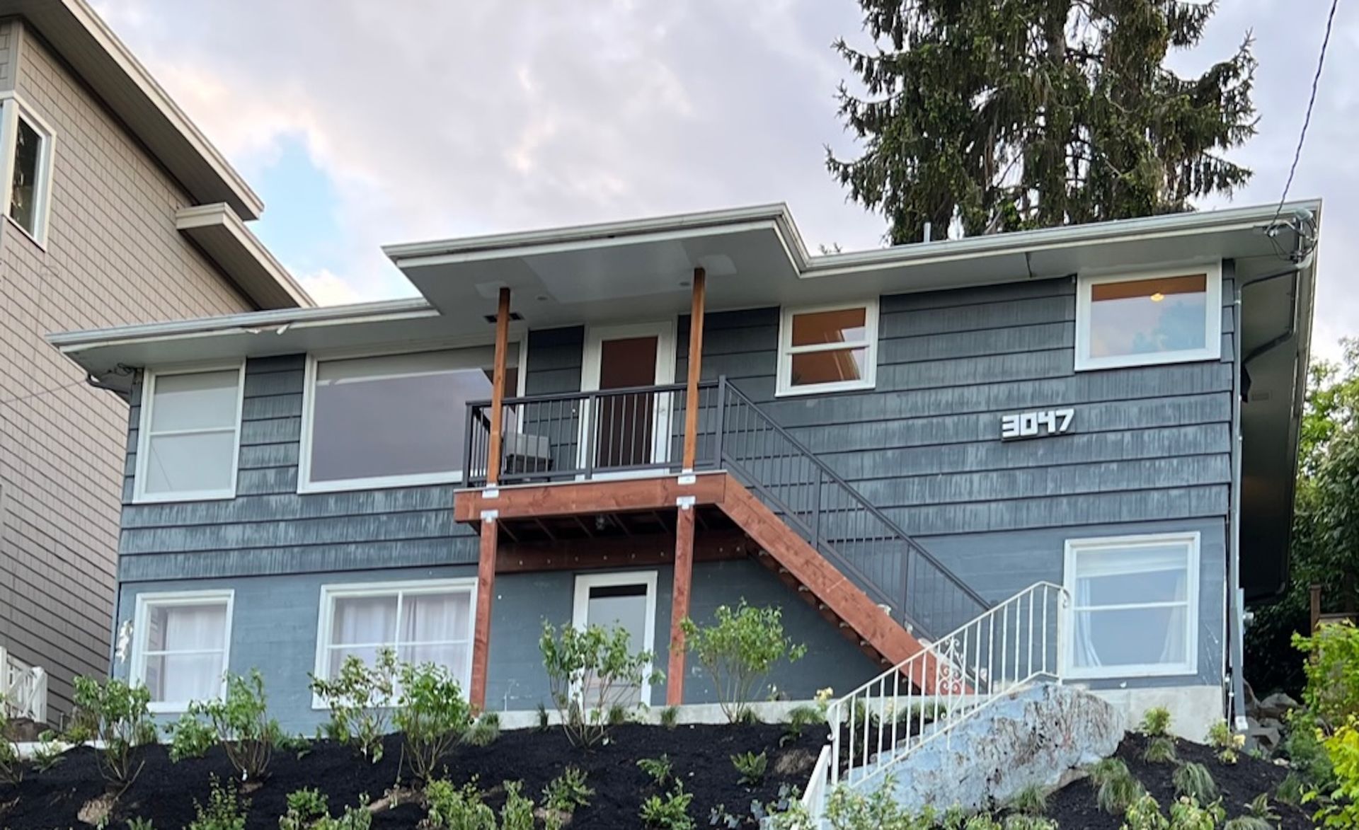 Blue-gray two-story house with orange stairs and white railings on a hillside