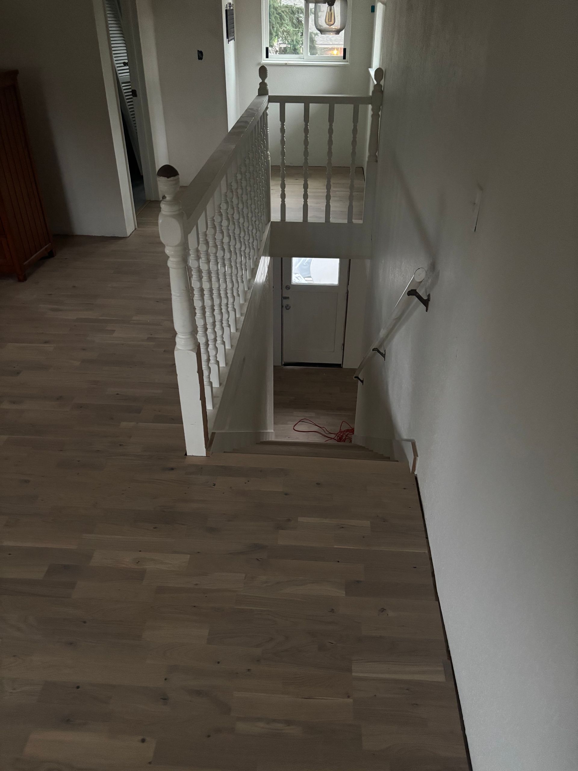 Hallway with wooden floor and white railing overlooking a staircase landing