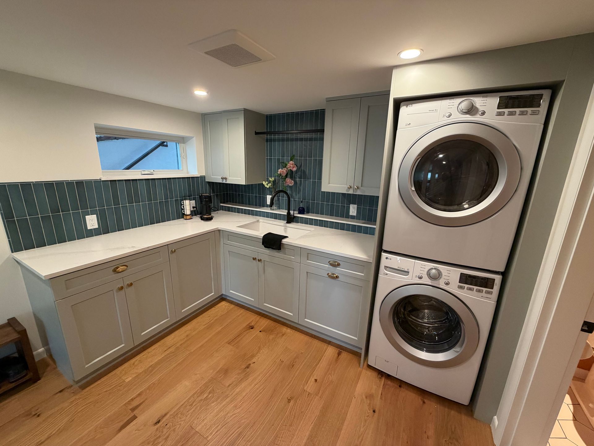 Compact laundry room with white cabinets, teal tile backsplash, stacked washer and dryer, and wood floor