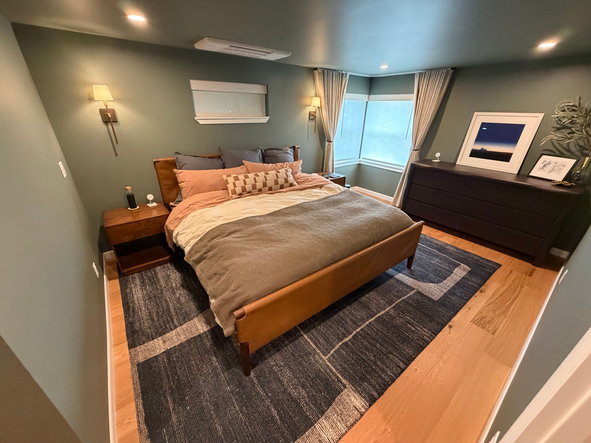Small bedroom with a made bed, gray walls, wood furniture, and a window with curtains.