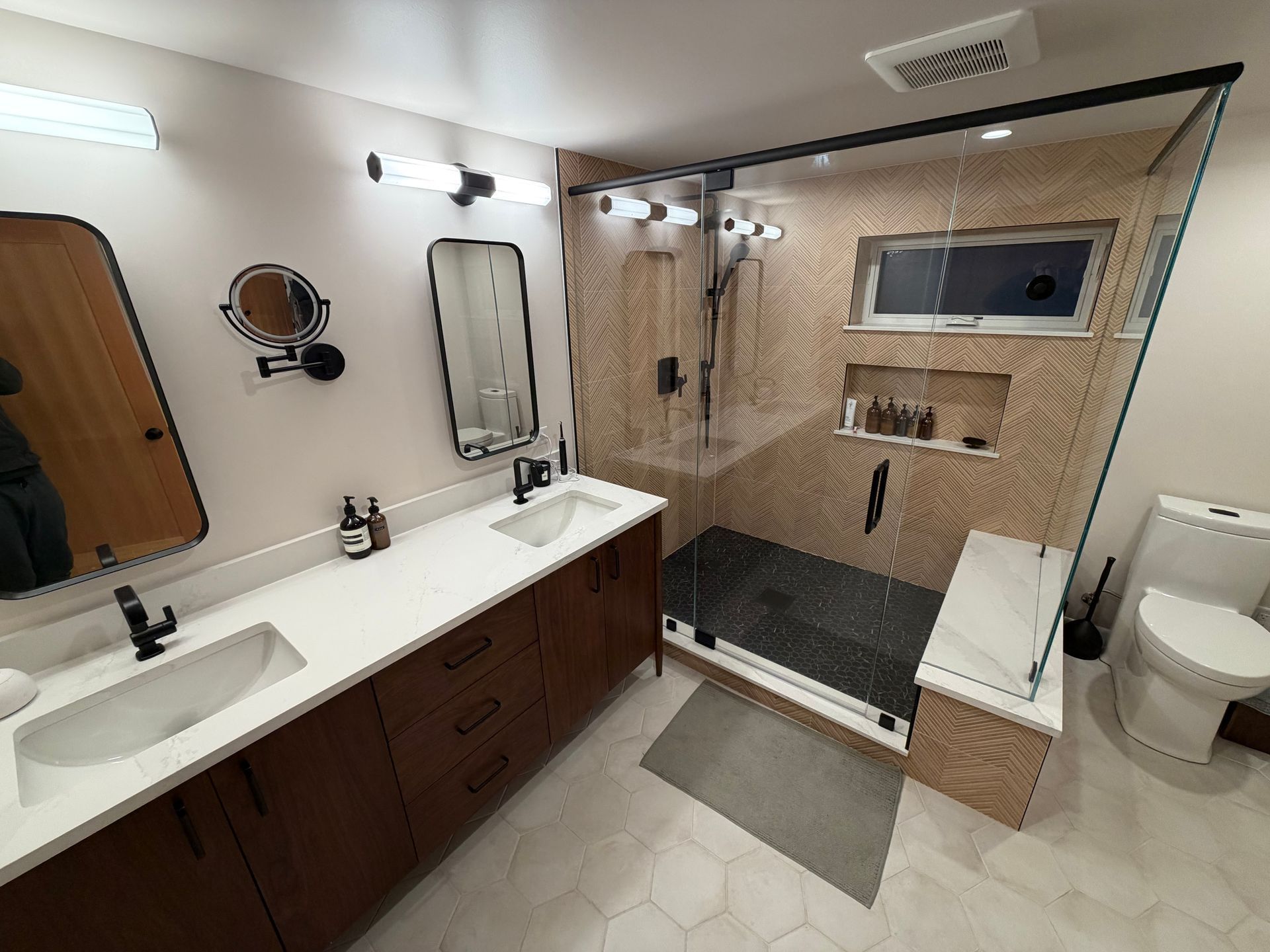 Spacious modern bathroom with double vanity, glass shower, white tile floor, and toilet.