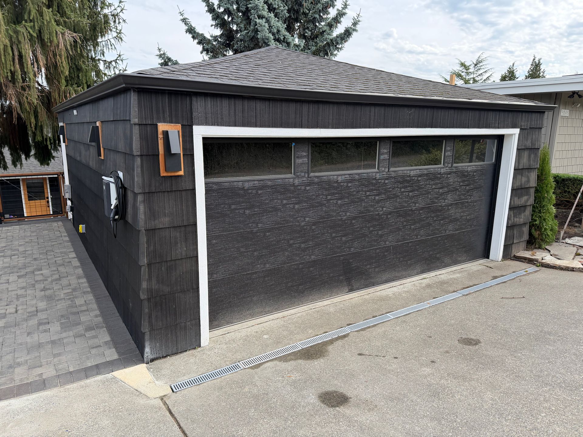 Detached black garage with a single large door and white trim beside a paved driveway