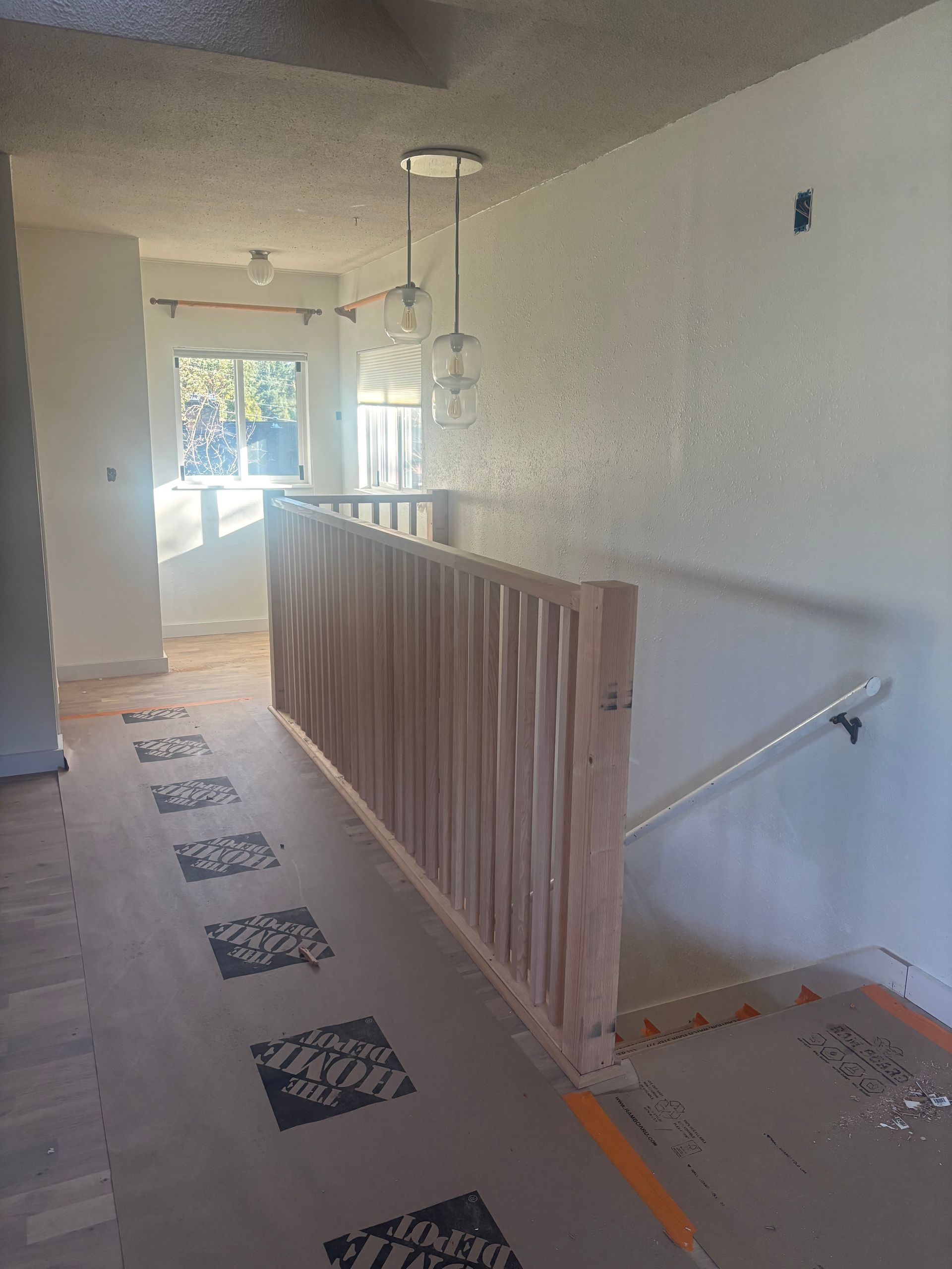 Hallway with a wooden stair railing, pendant lights, and bright windows at the far end.