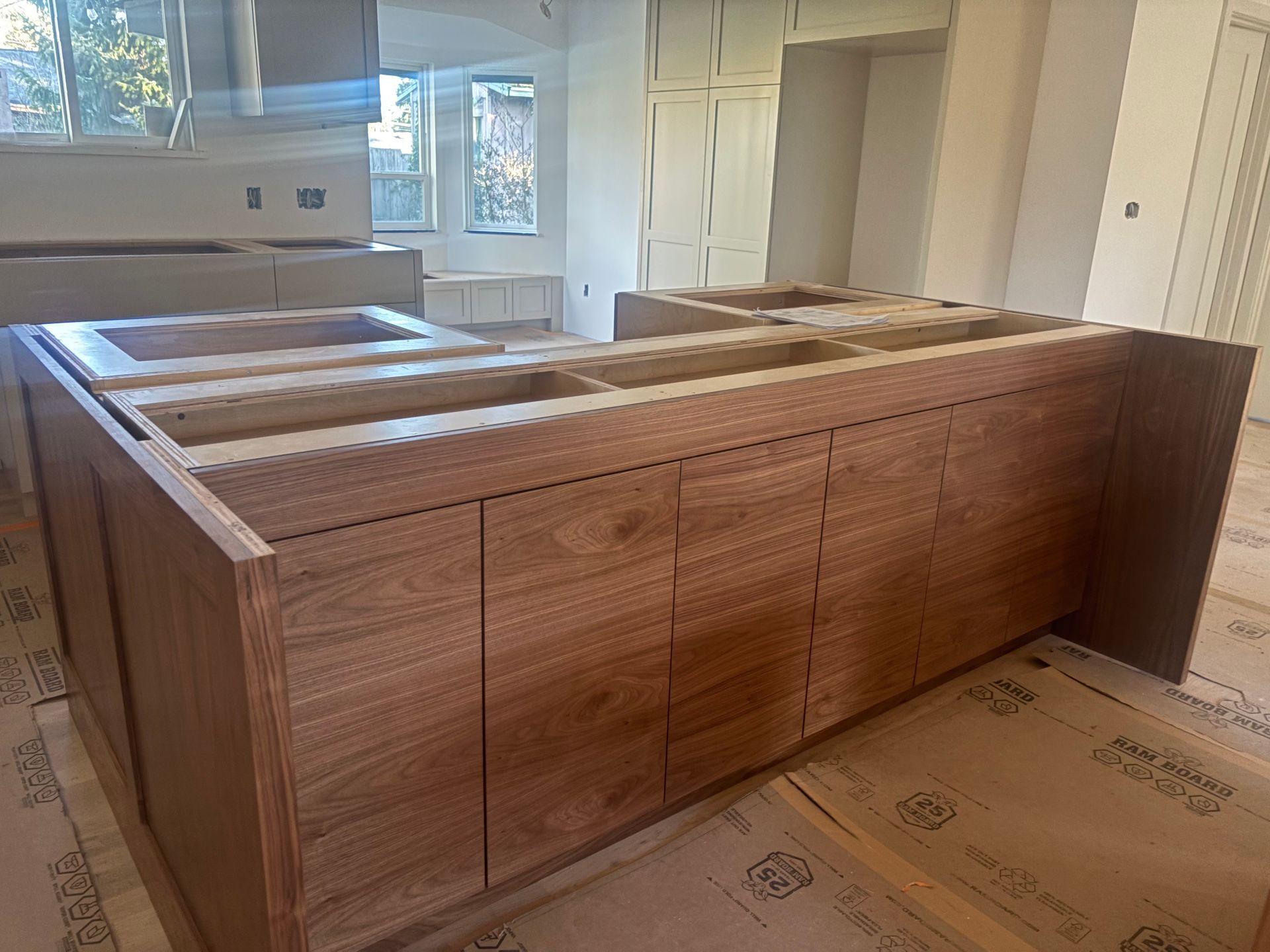 Unfinished wood kitchen island cabinets in a bright room with windows and cardboard floor protection
