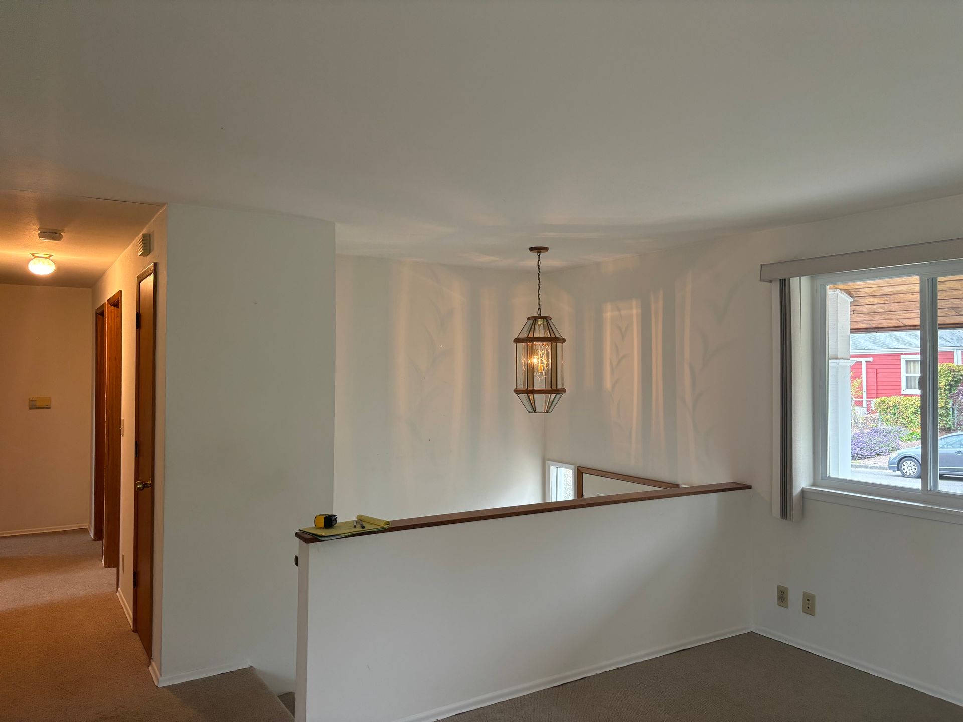Empty hallway and stair landing with white walls, hanging lantern, and a window overlooking outside.