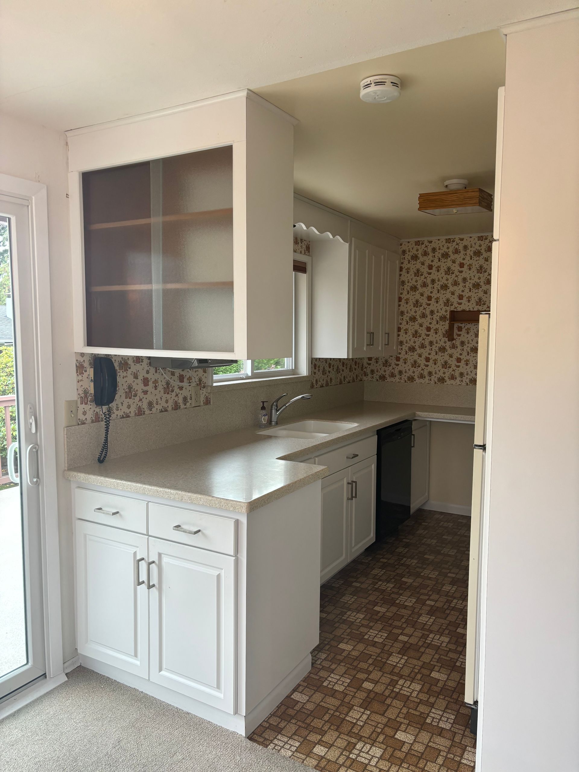 Bright white kitchen with mosaic backsplash, glass-front cabinets, and tiled floor near a sliding glass door