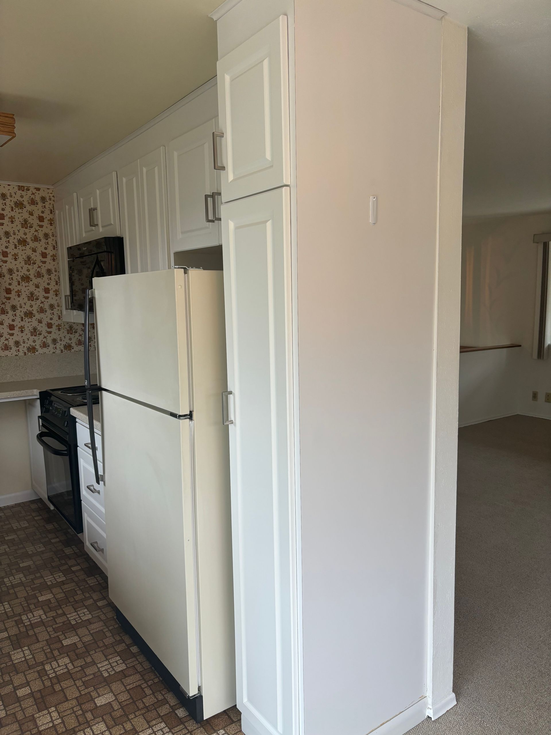 Narrow kitchen view with white appliances and cabinets beside a hallway doorway