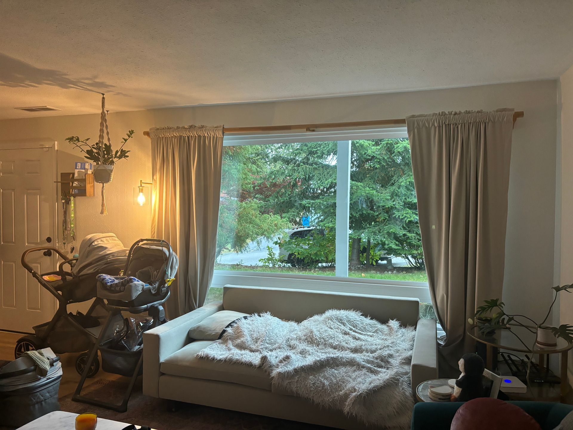 Cozy living room with a sofa by a large window, curtains, warm lamp light, and an exercise bike on the left.
