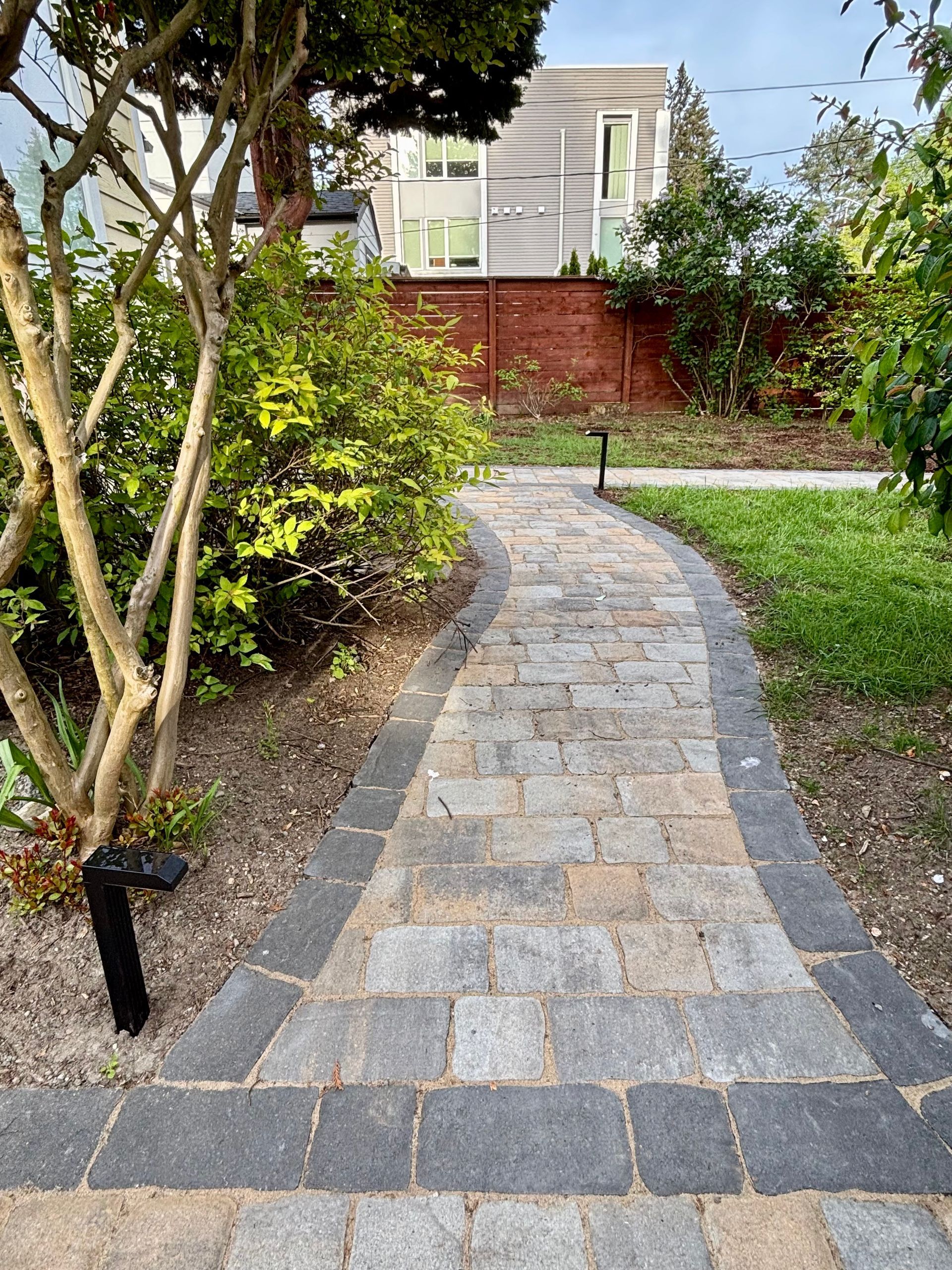 Curved stone walkway through a landscaped garden leading to a house in the background