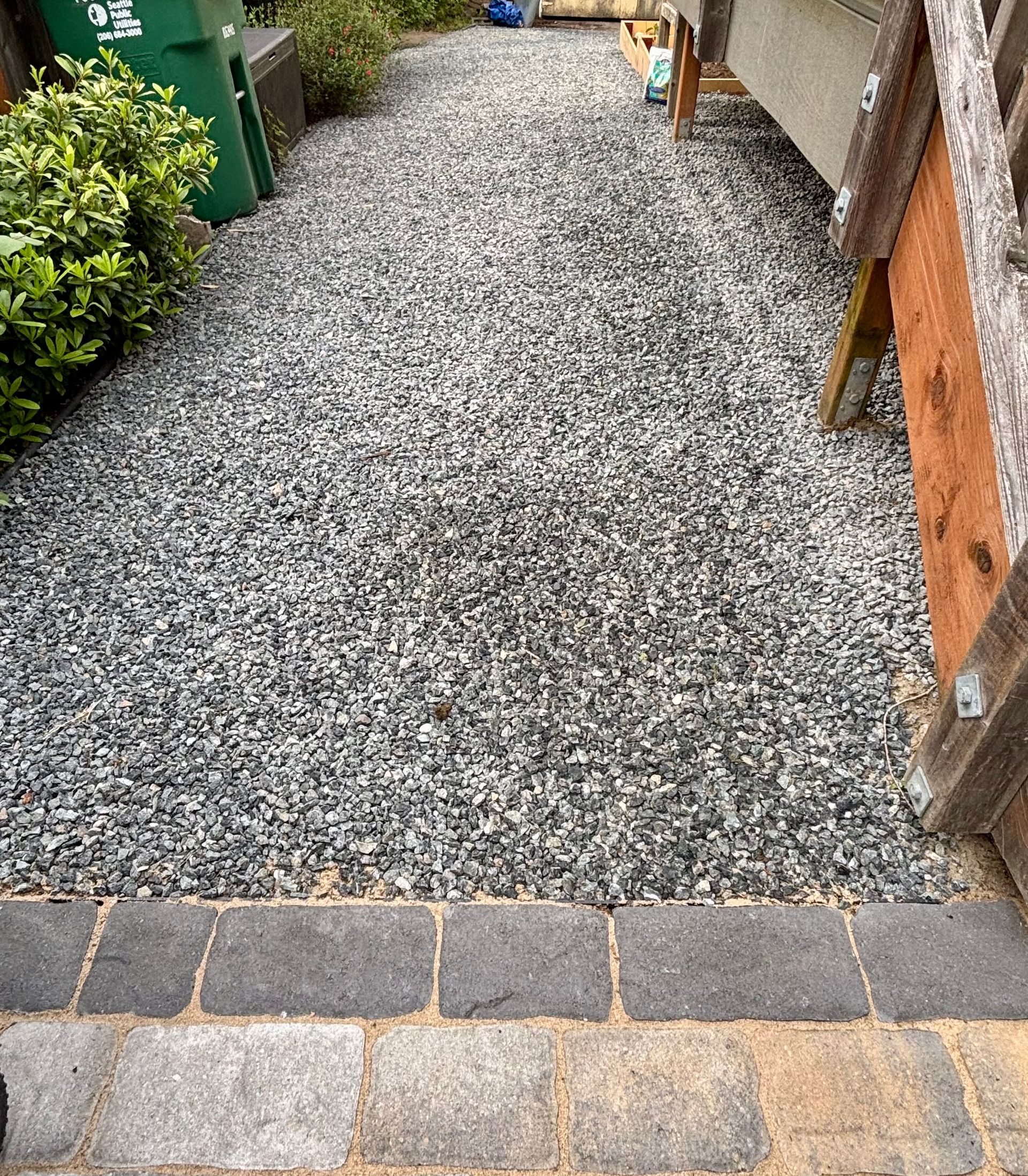 Gravel garden path bordered by plants and wood, leading from a stone-paved threshold