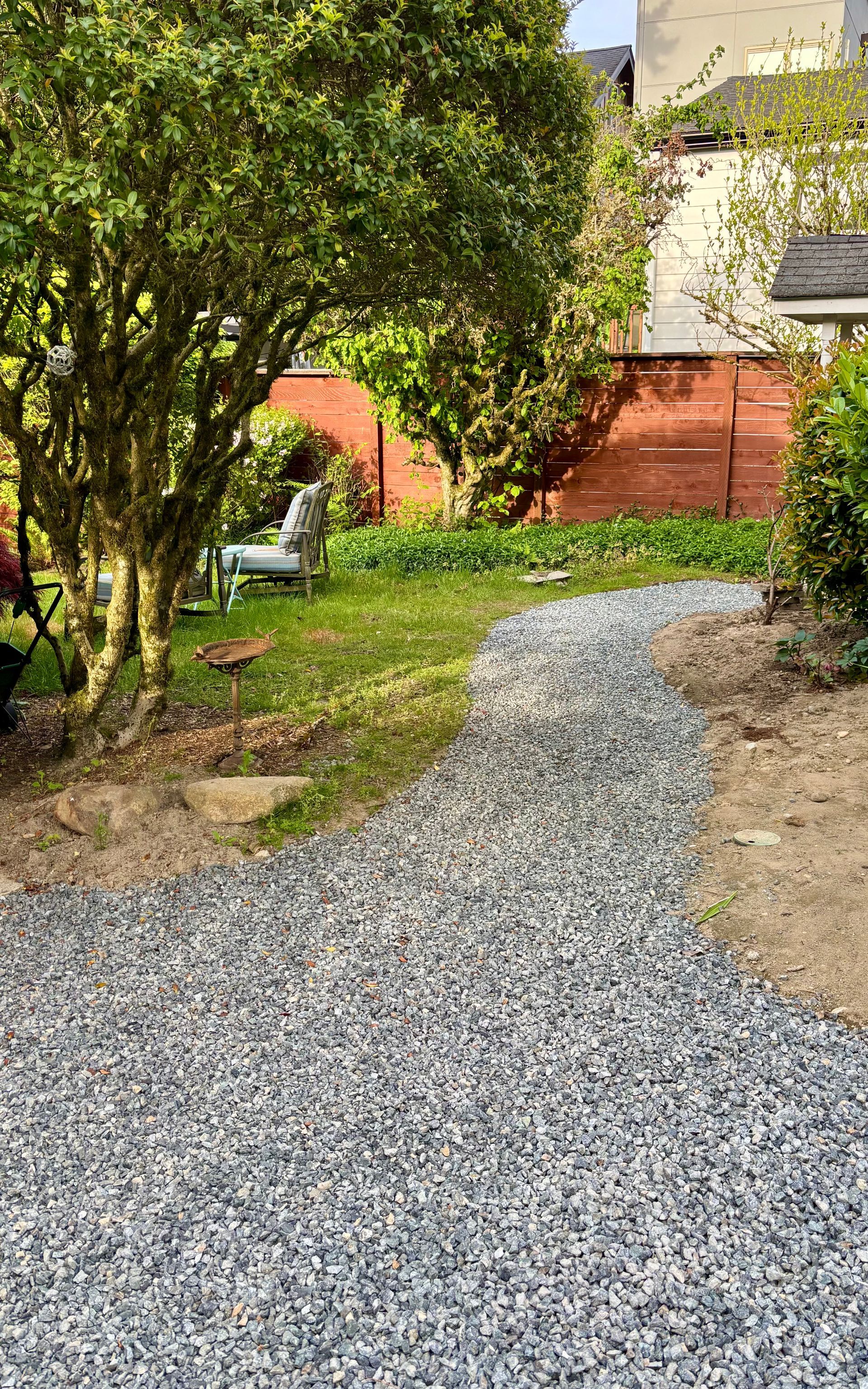 Gravel path curving through a leafy garden beside a red fence and trees