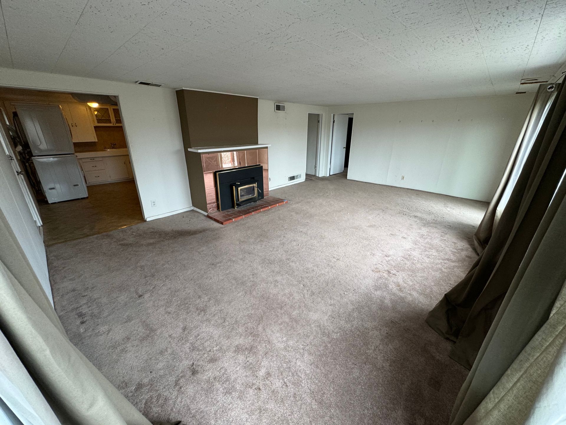 Empty carpeted living room with fireplace, sliding glass doors, and an open doorway to the kitchen