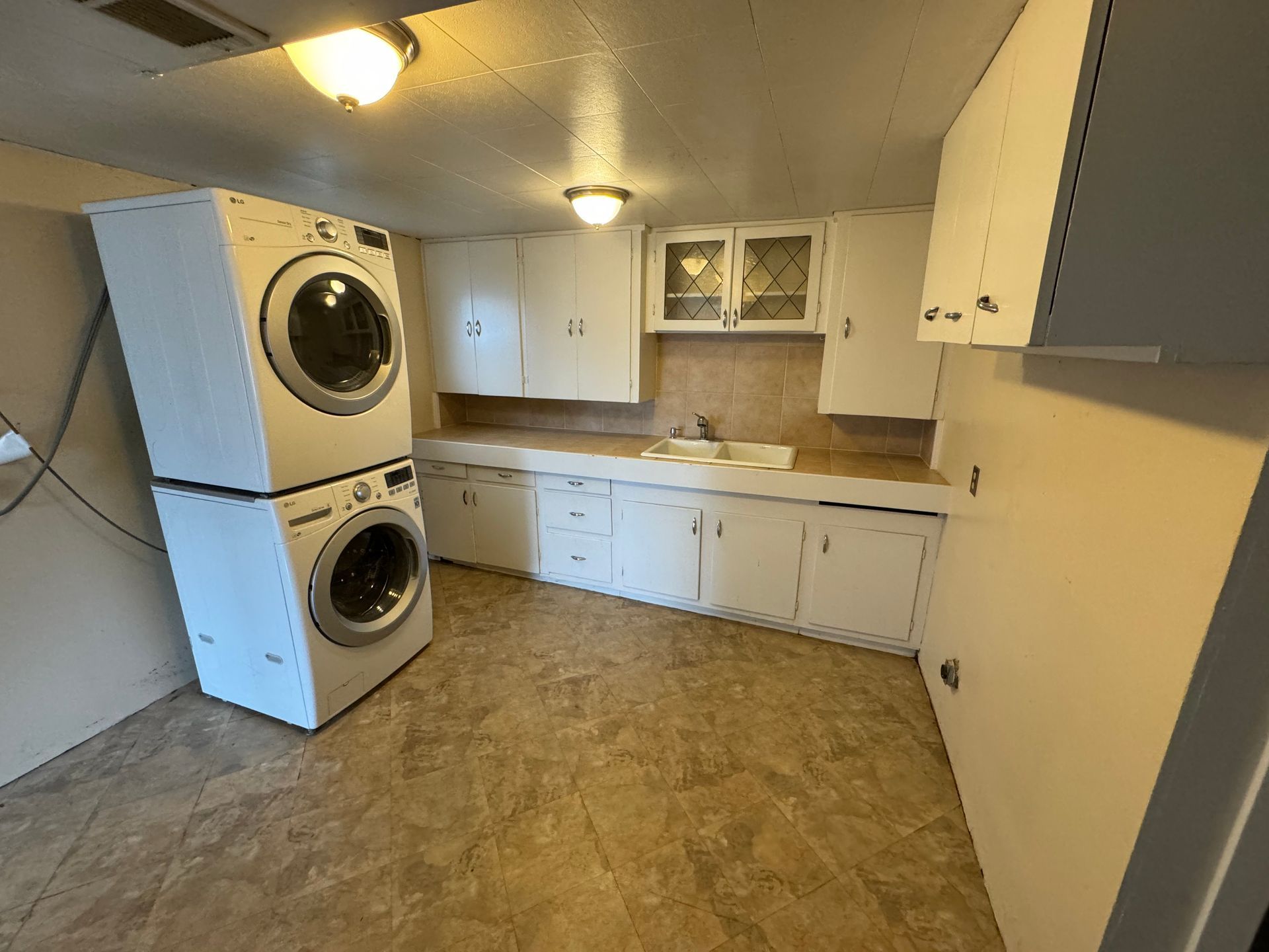 Small kitchen with white cabinets, wood countertops, stacked washer/dryer, and beige vinyl floor.