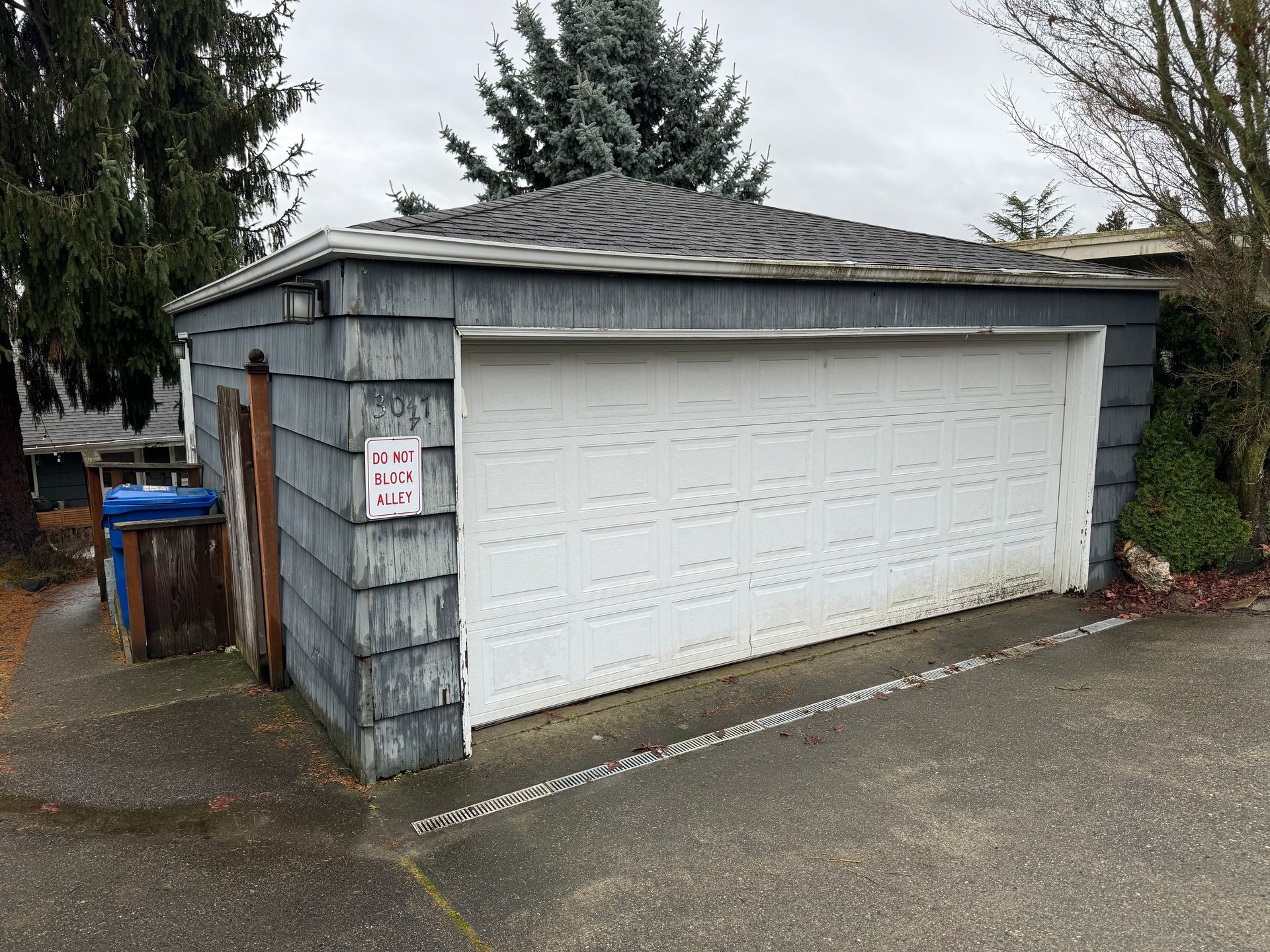 Detached gray garage with white double doors and a small sign beside the driveway