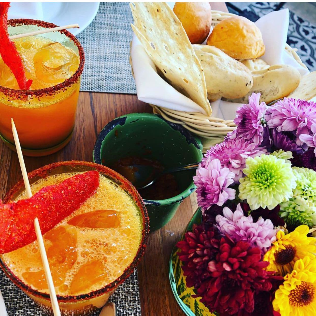 Una mesa con bebidas, flores y pan.
