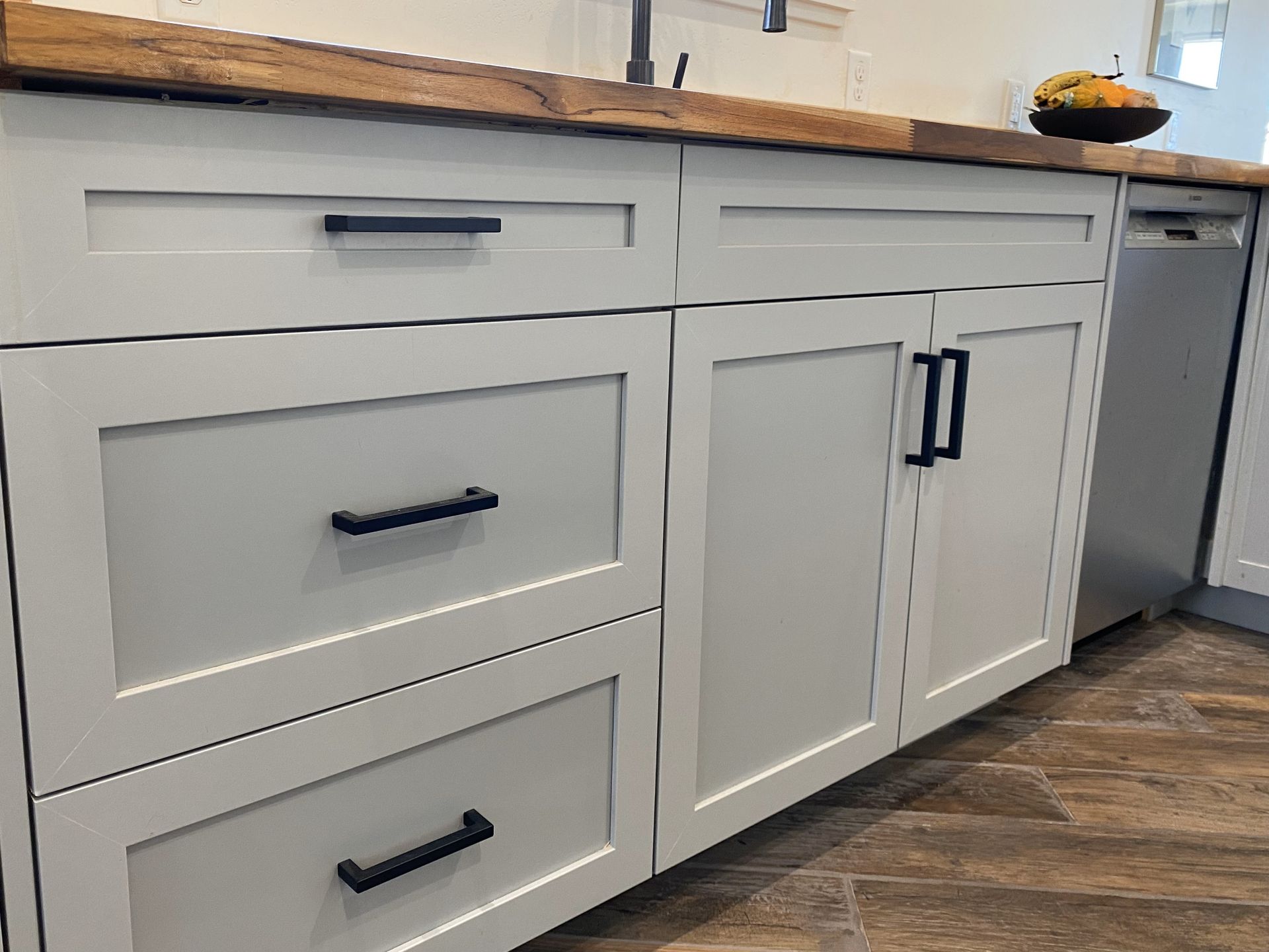 A kitchen with white cabinets and black handles and a wooden counter top.