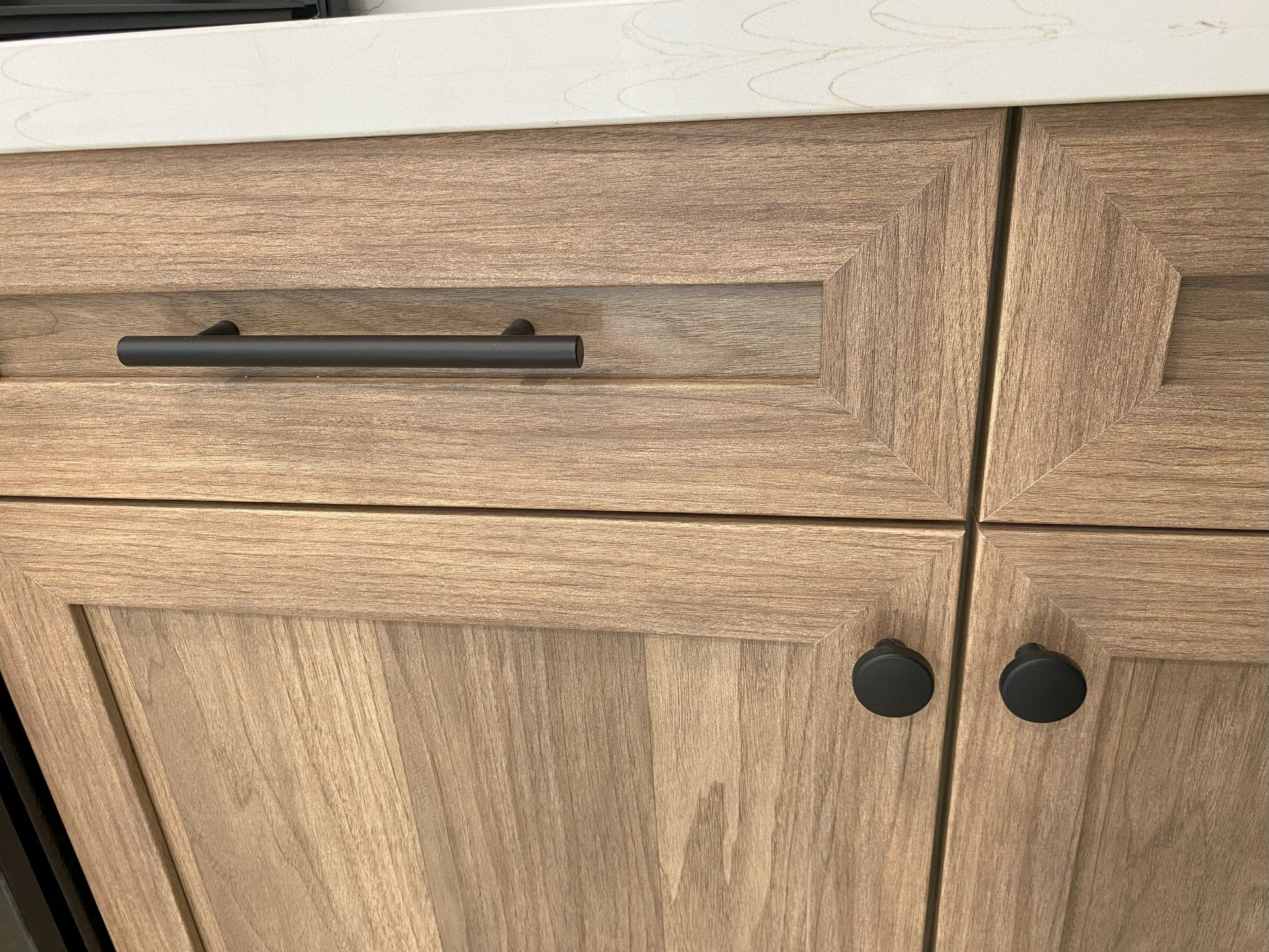 A close up of a wooden cabinet with black handles and knobs.