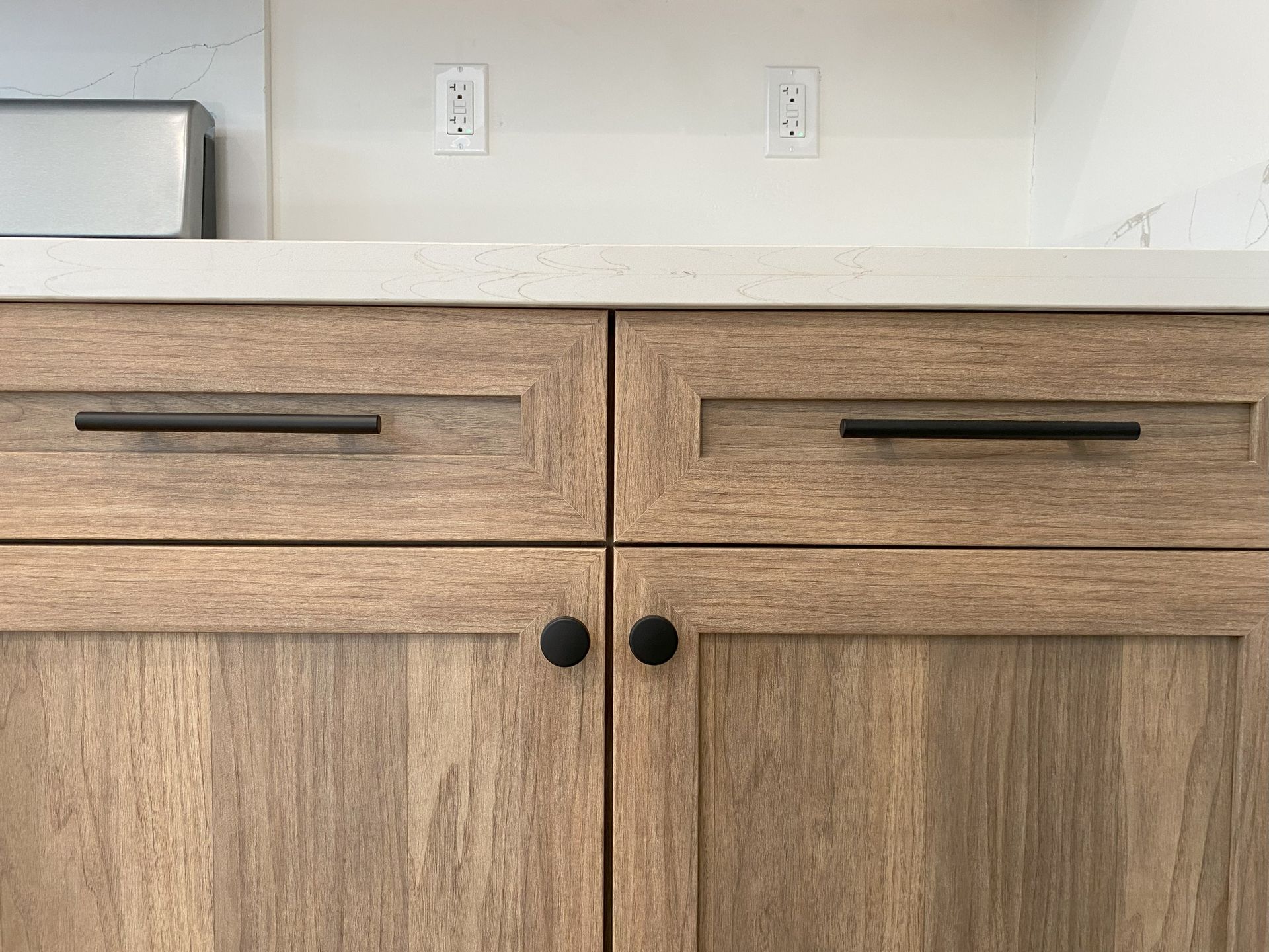 A close up of a kitchen counter with wooden cabinets and black handles.