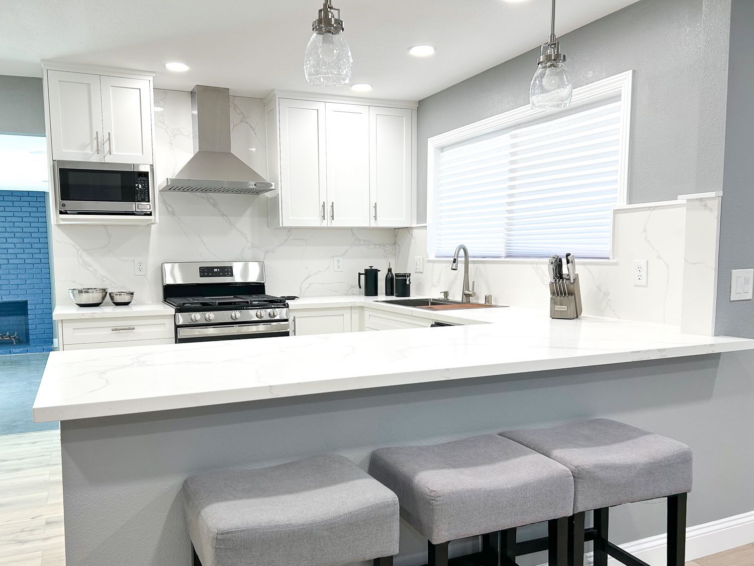 Modern white kitchen with countertop seating, stainless steel appliances, and gray accents.