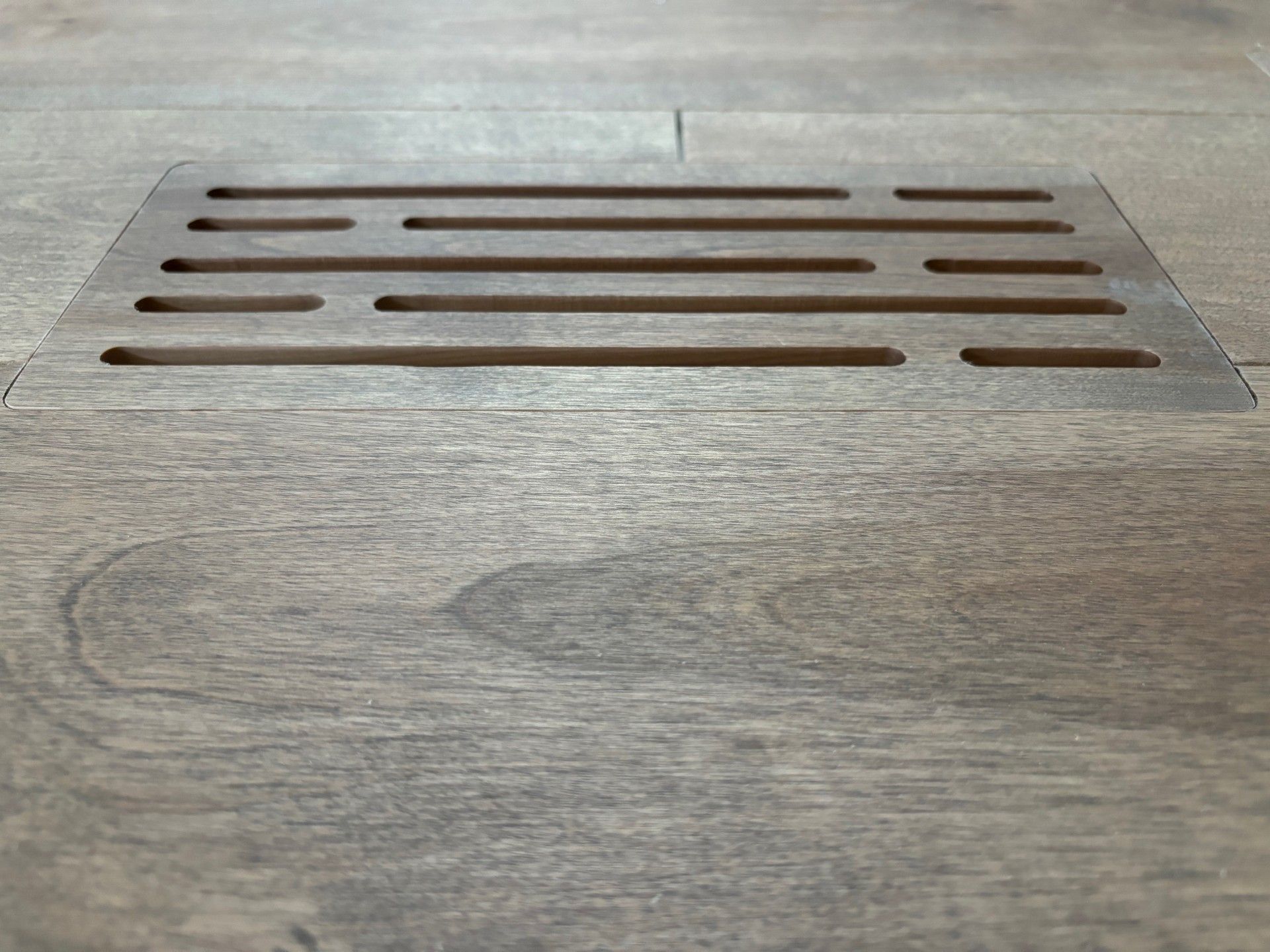Grille d'aération de plancher en bois avec fentes horizontales, encastrée dans un plancher à grain de bois.