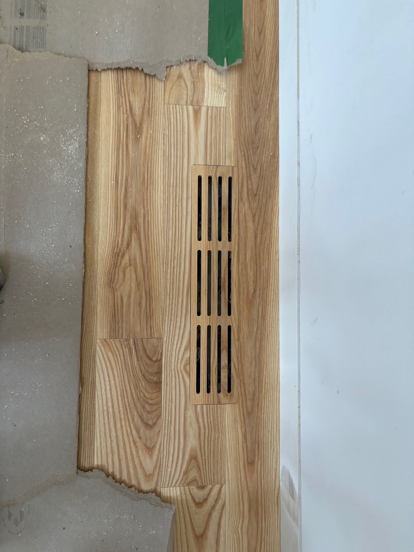 Plancher en bois avec aération, adossé à un mur et à une dalle de béton brut.