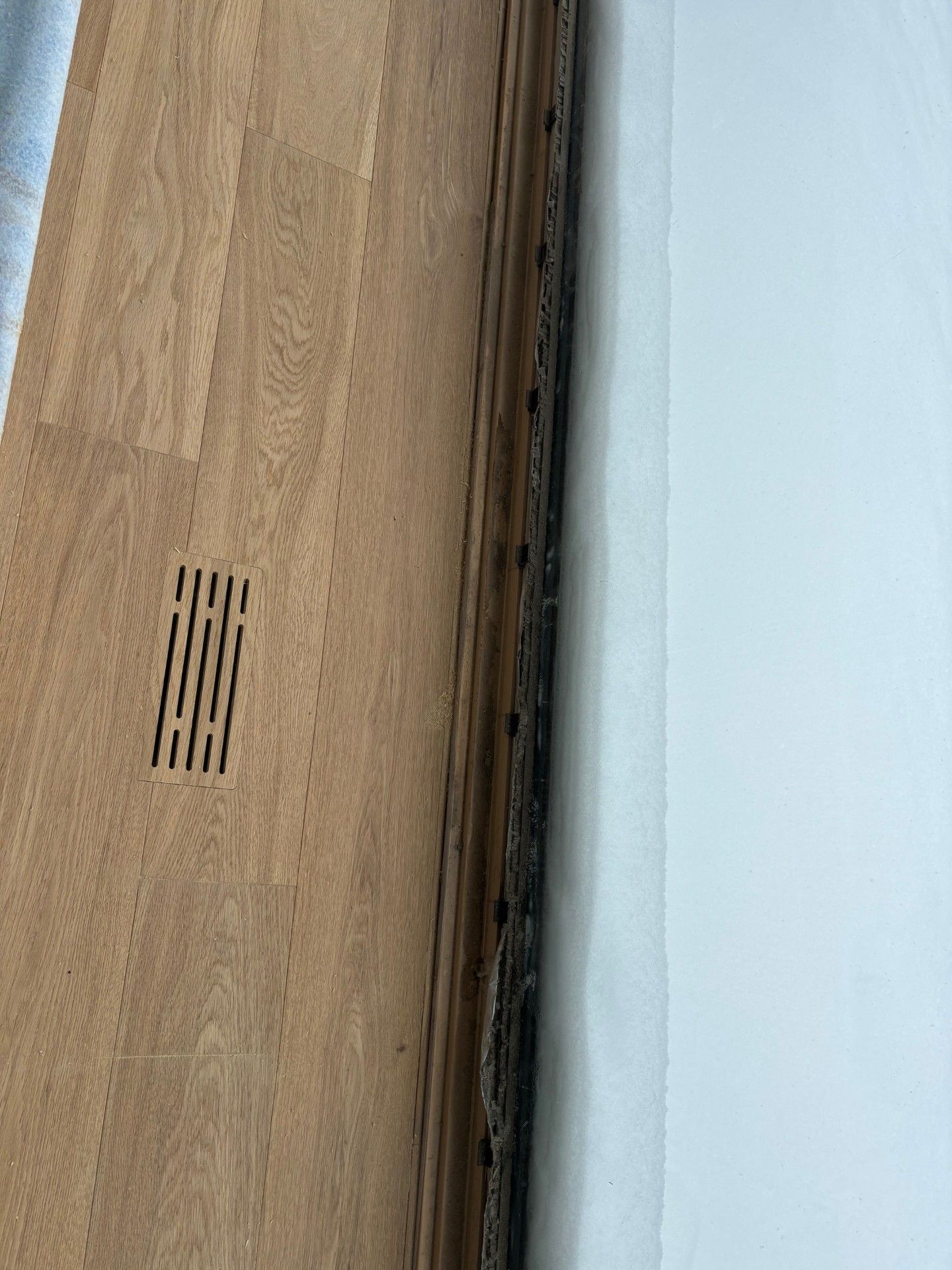 Parquet jouxtant un mur blanc présentant une décoloration foncée sur le pourtour.