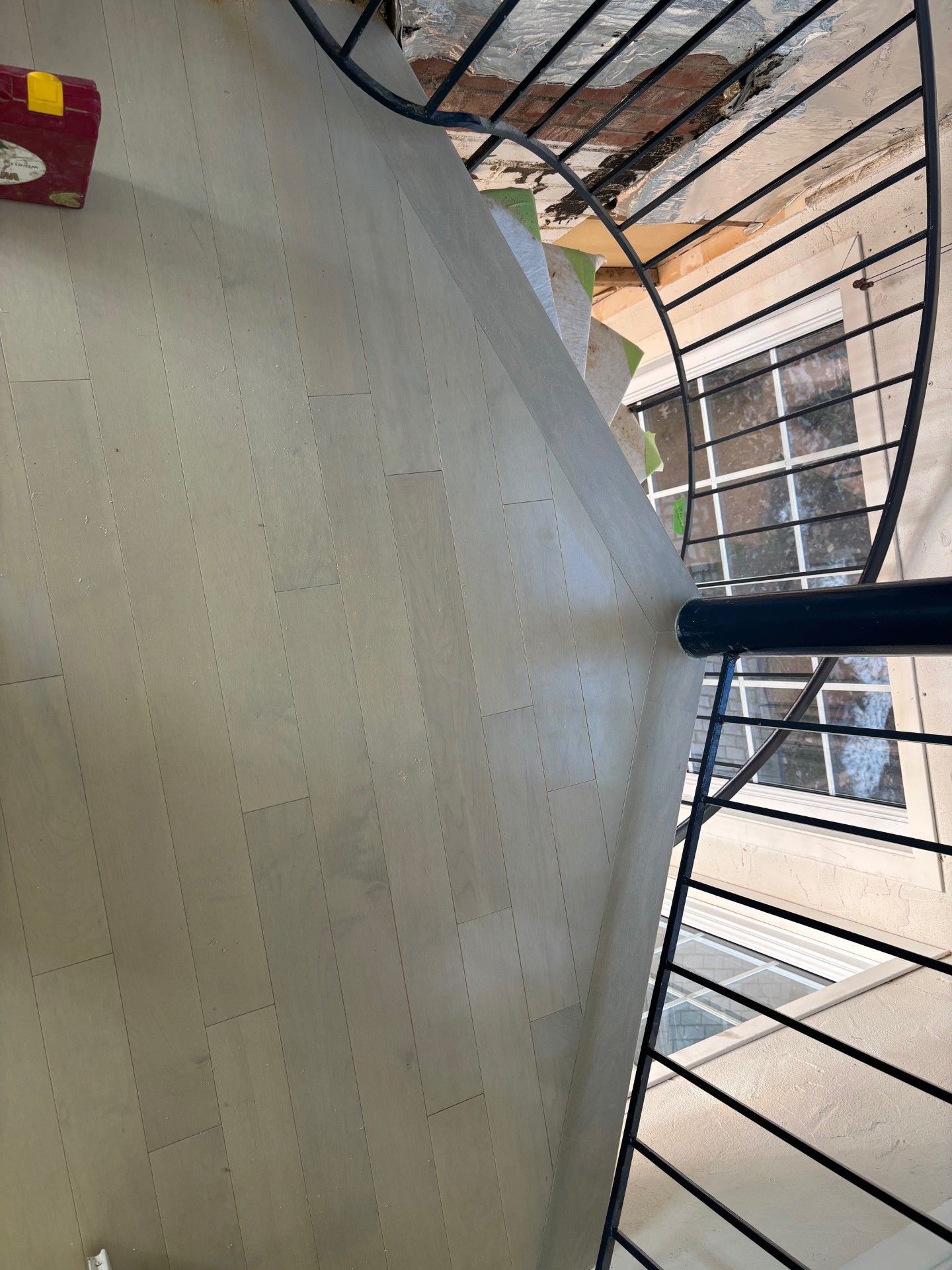 Un escalier en colimaçon avec une rampe en métal monte, le sol gris clair étant percé de nombreux petits trous.