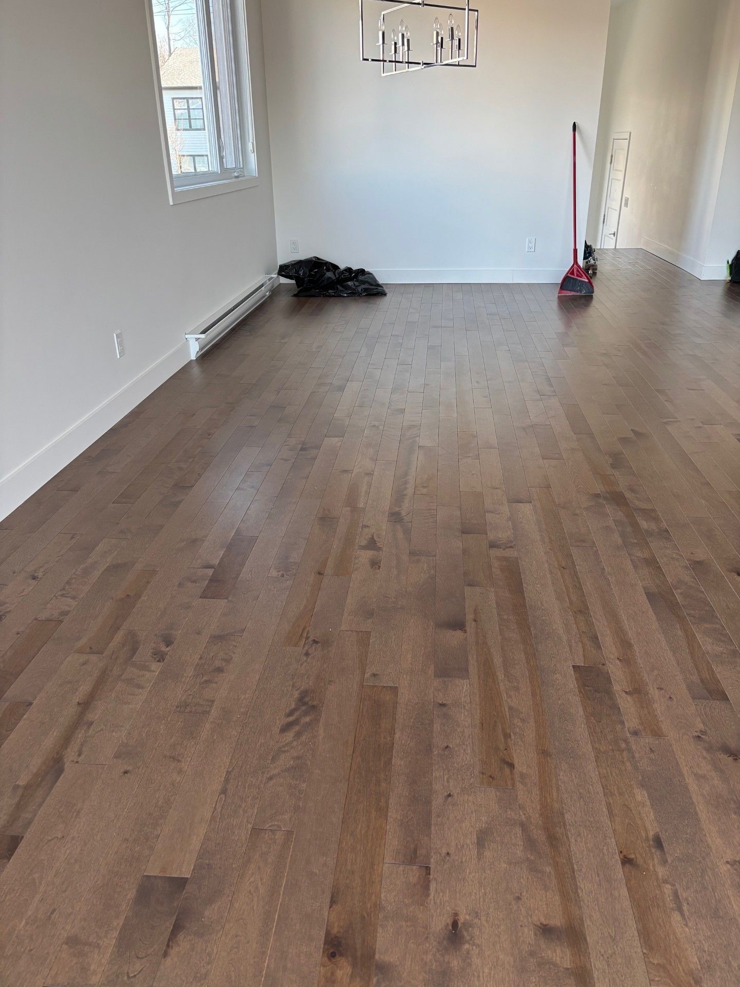 Pièce vide avec parquet marron, murs blancs et une fenêtre.