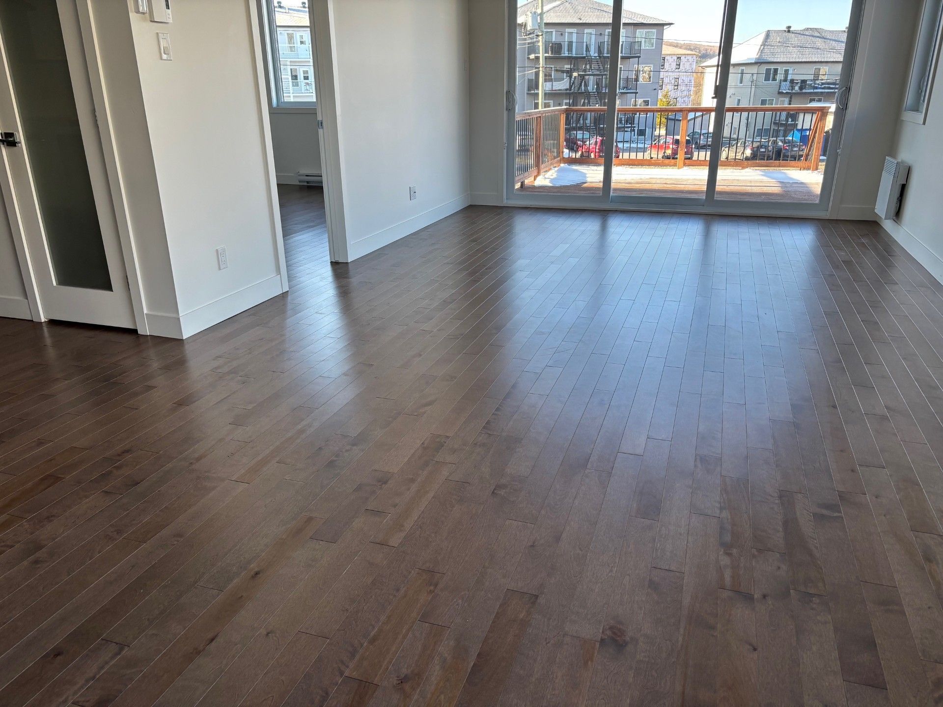 Plancher de bois franc dans une pièce lumineuse avec une grande fenêtre et une vue sur un paysage urbain.