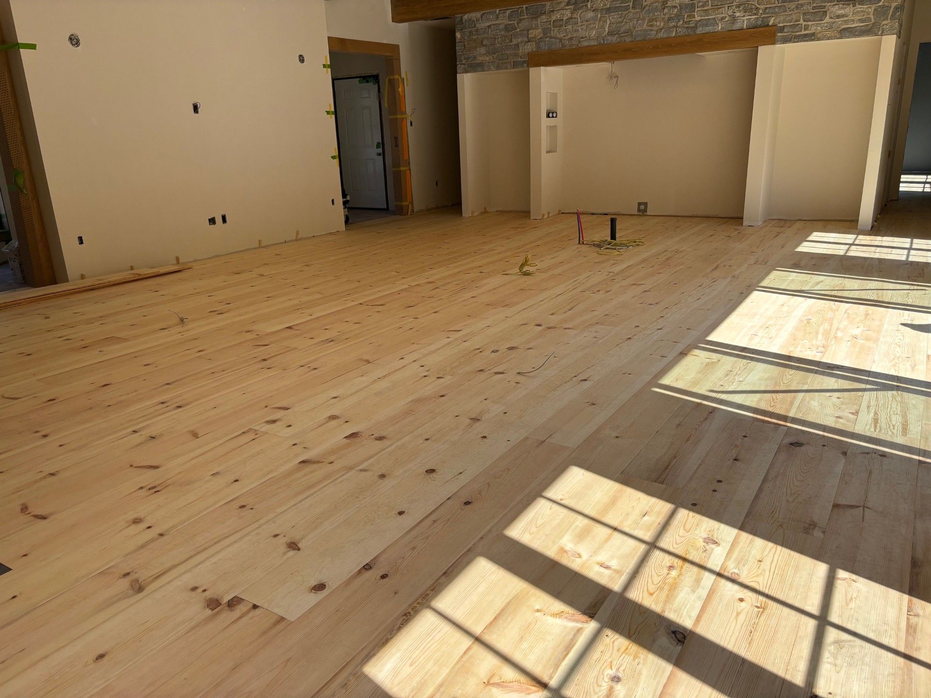 Plancher en bois clair nouvellement installé dans une pièce aux murs non finis et baignée de lumière naturelle.