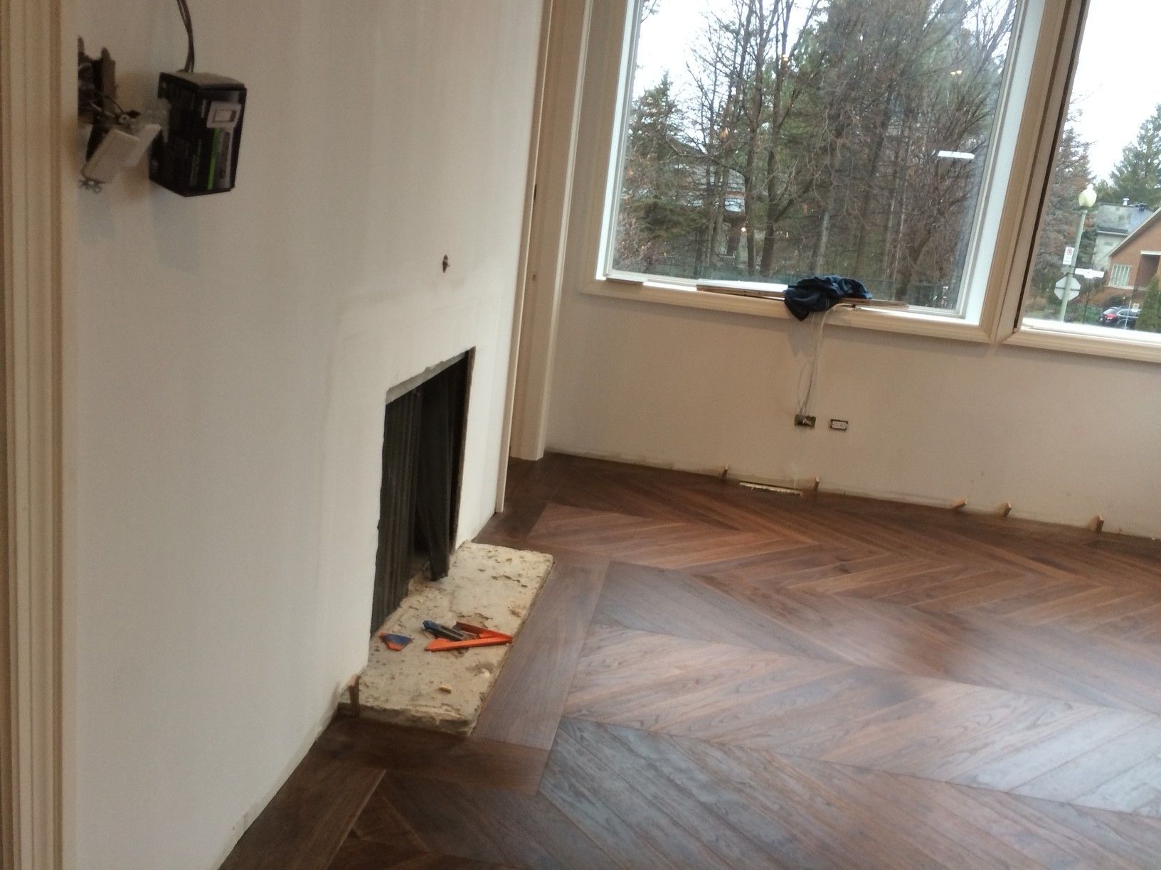 Chambre avec parquet neuf, cheminée et grande fenêtre donnant sur les arbres.