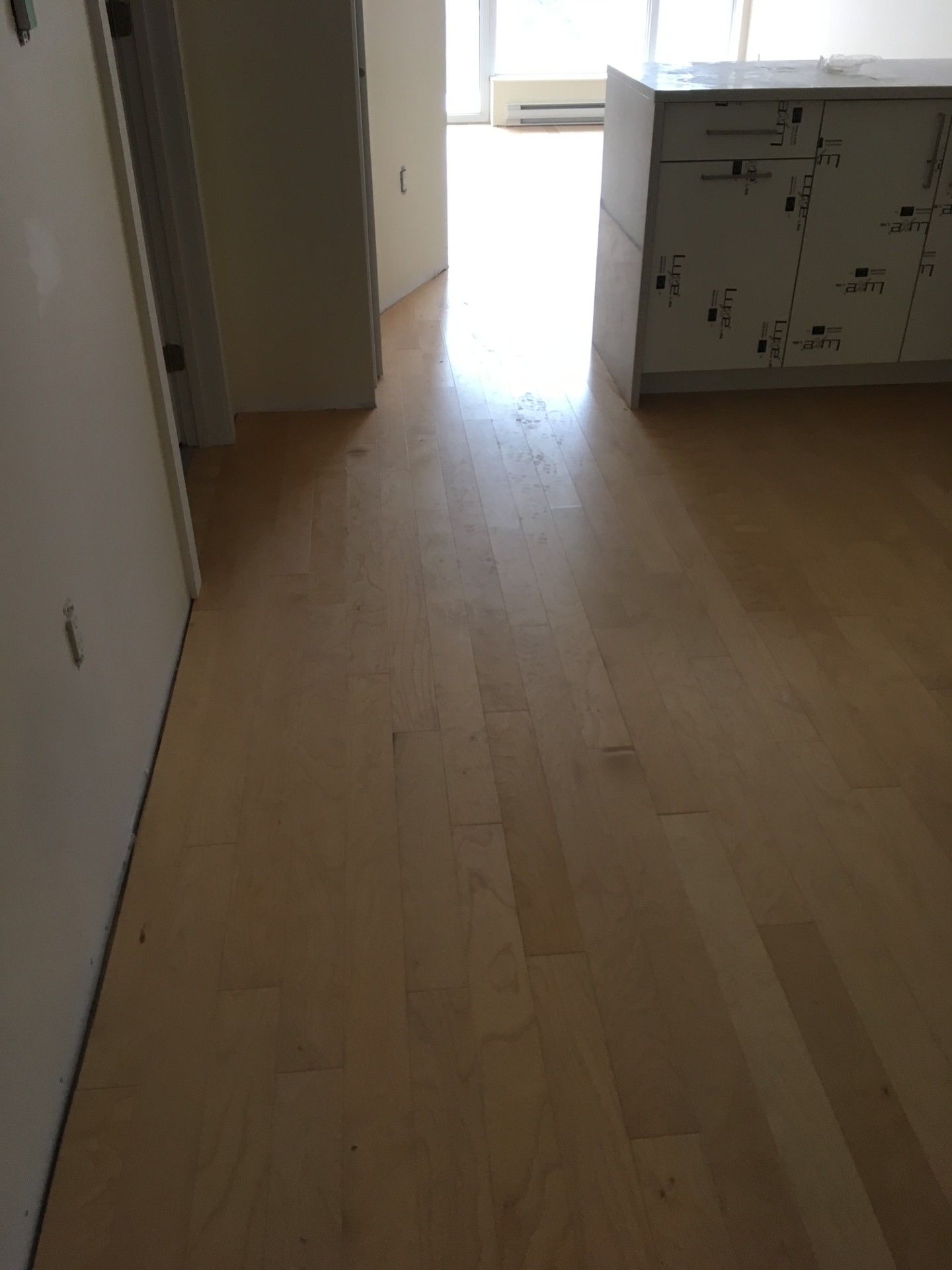 Un parquet clair mène à un espace ouvert et lumineux. Un meuble blanc se trouve à droite et une porte à gauche.