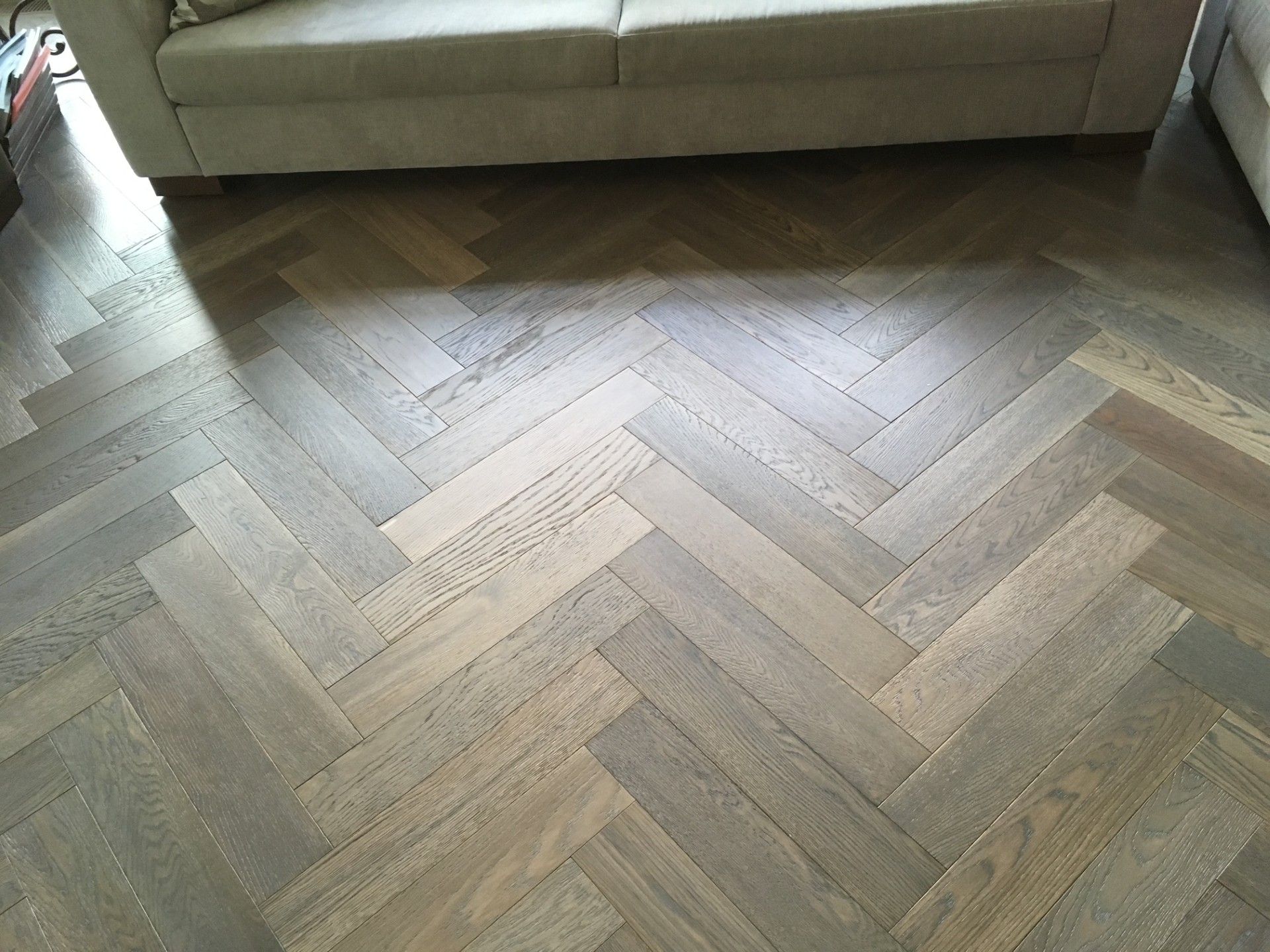 Sol en bois à chevrons dans des tons neutres, avec un canapé visible en arrière-plan.