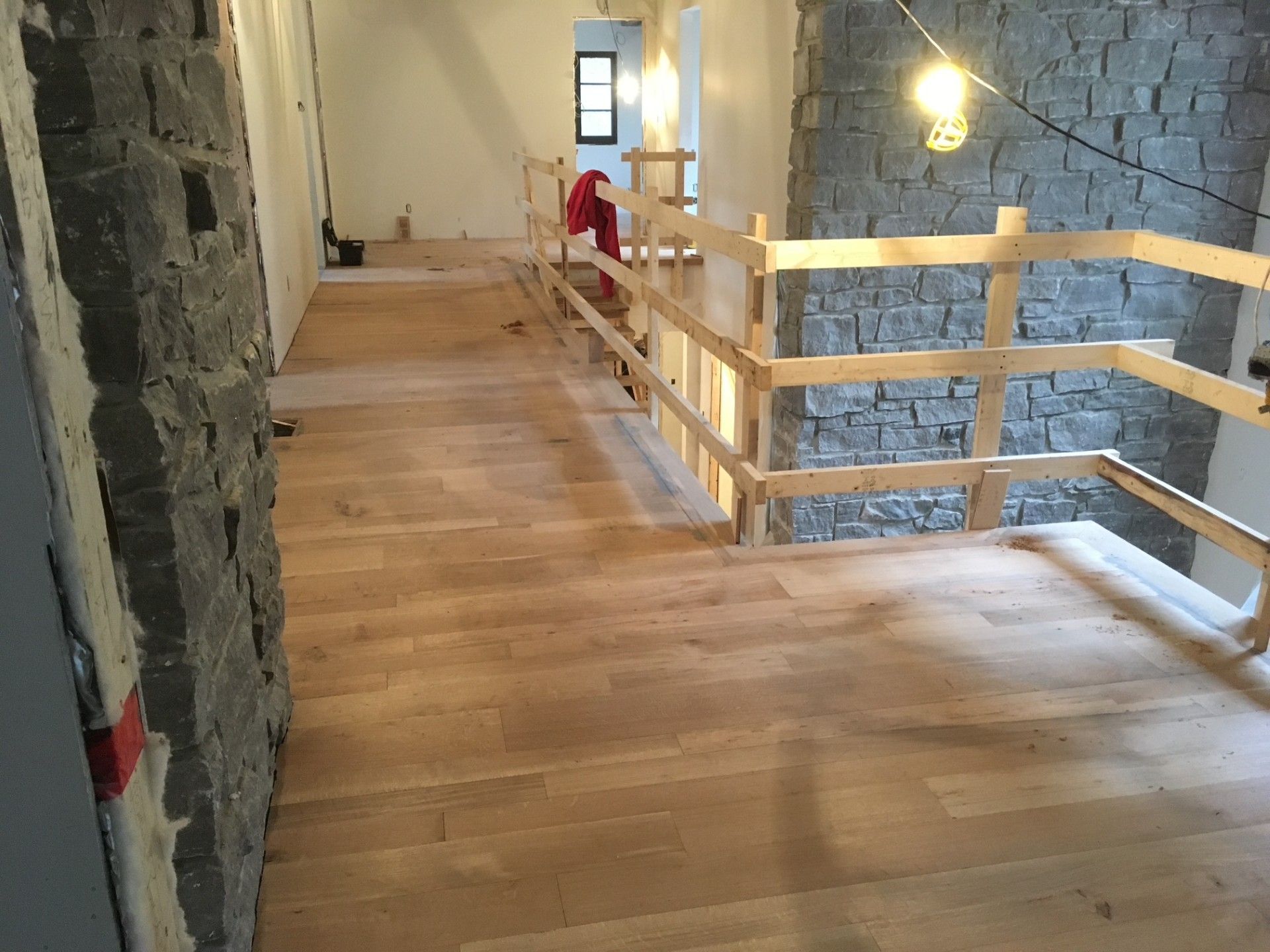 Sol en bois et rambarde provisoire dans un bâtiment en rénovation, avec des murs en pierre et une ampoule suspendue.