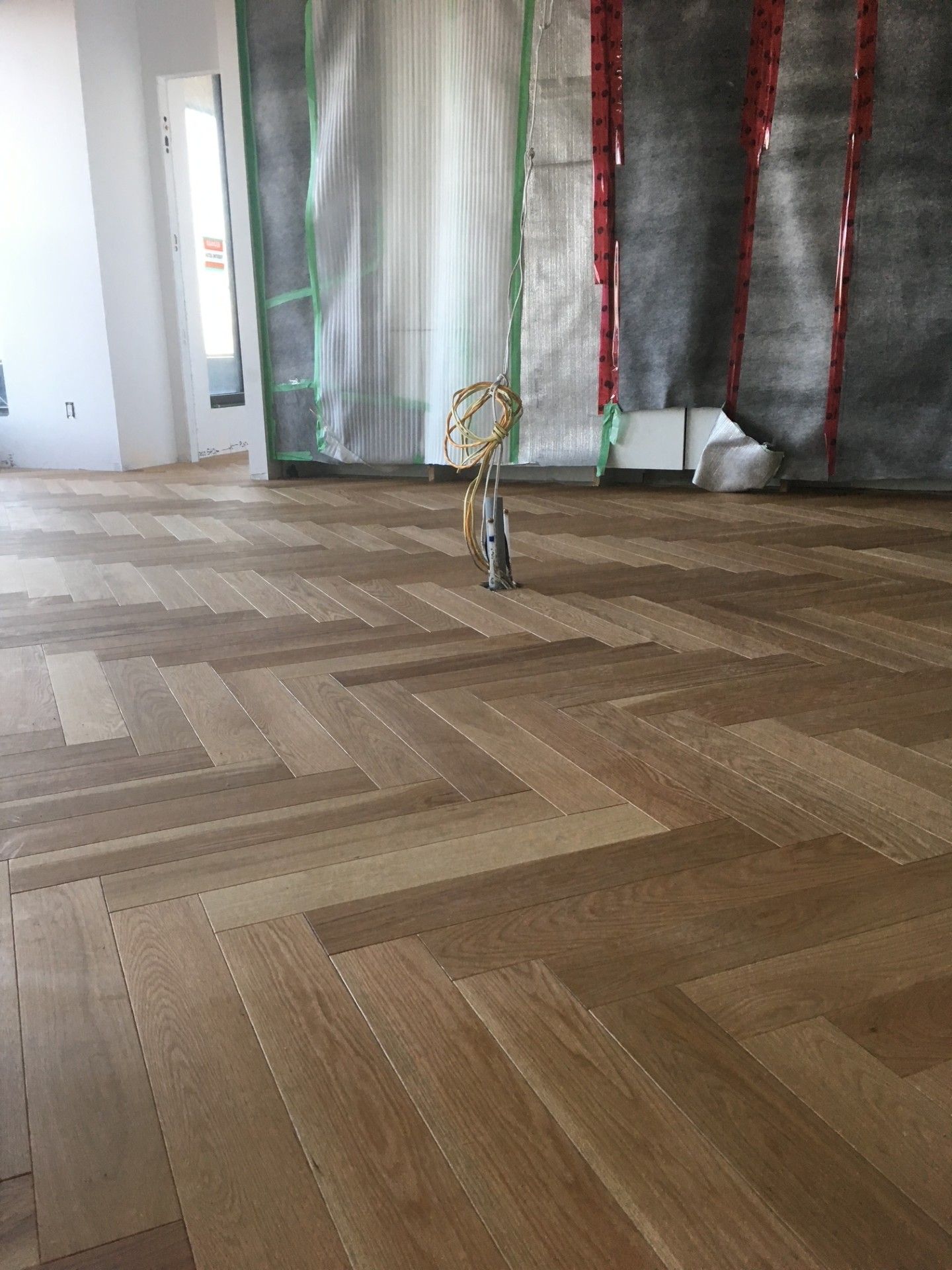 Parquet à chevrons dans une pièce en construction, avec une bâche en plastique sur le mur.
