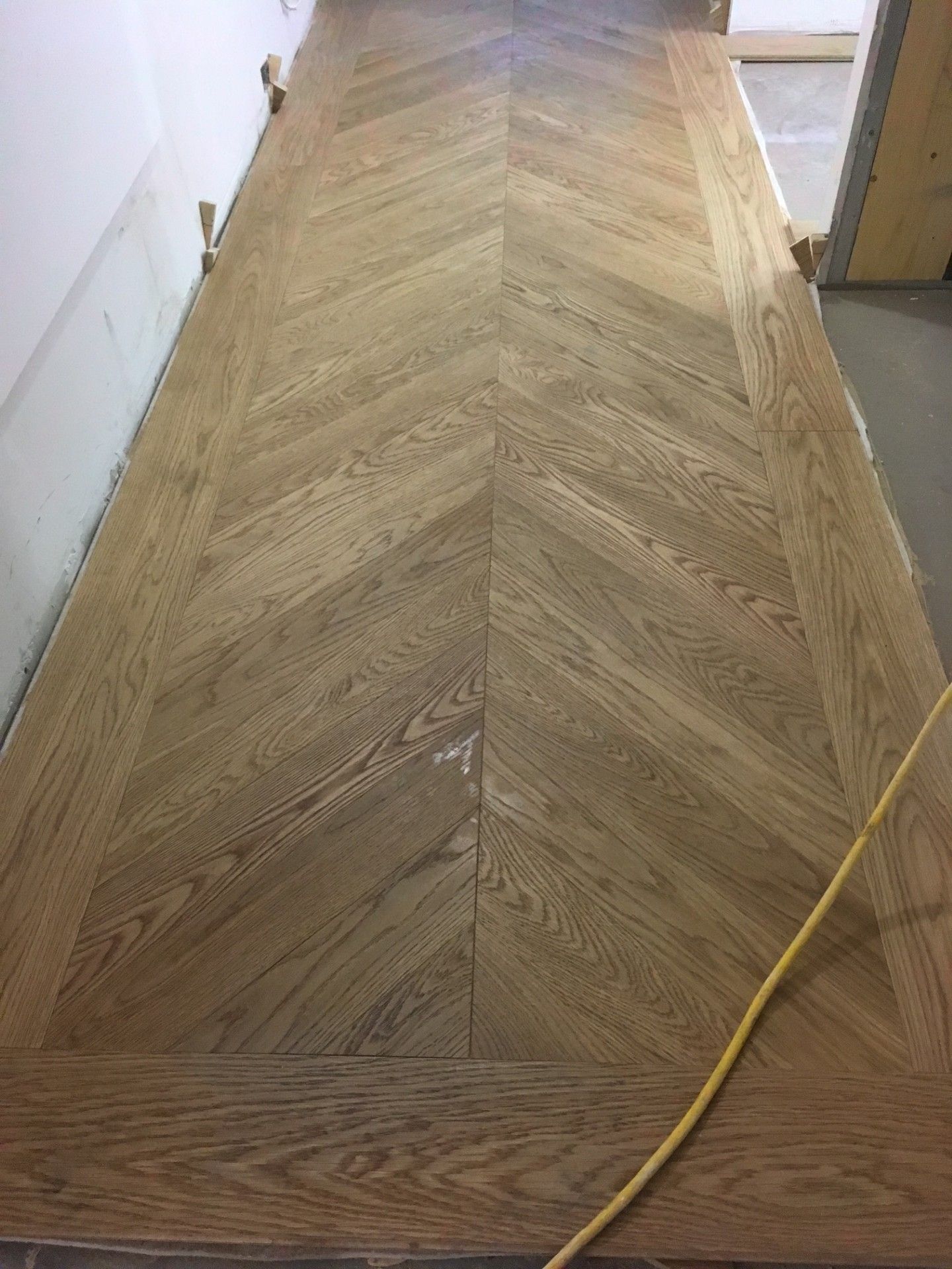 Parquet en bois à chevrons de couleur brun clair, avec un cordon jaune courant en bas à droite.