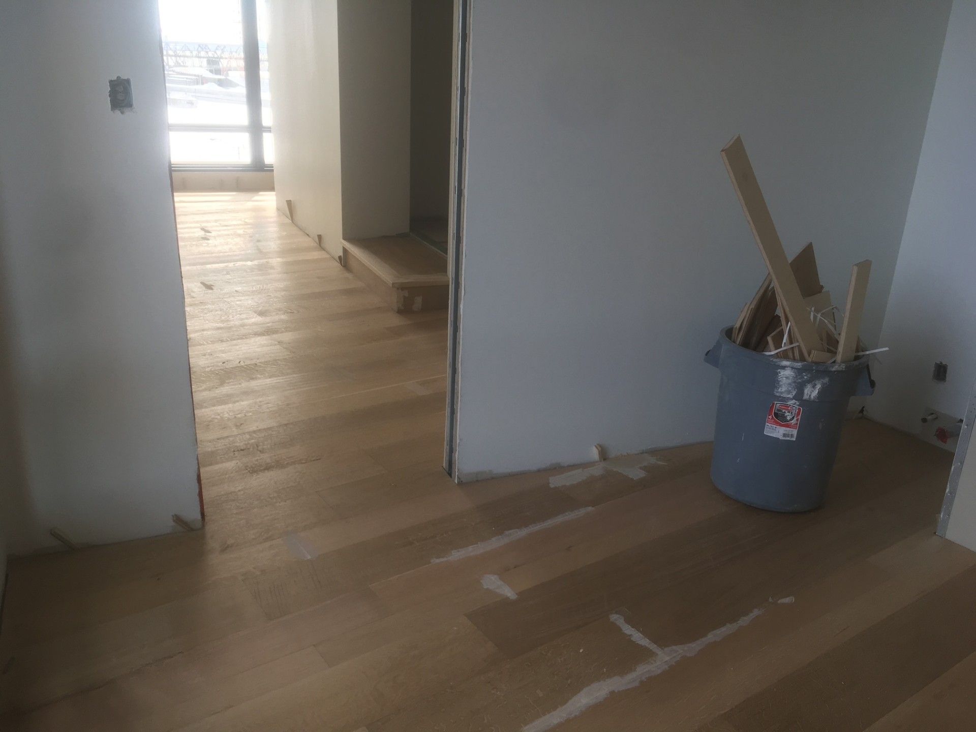 Pose de parquet dans une pièce en construction, avec une poubelle et des portes.
