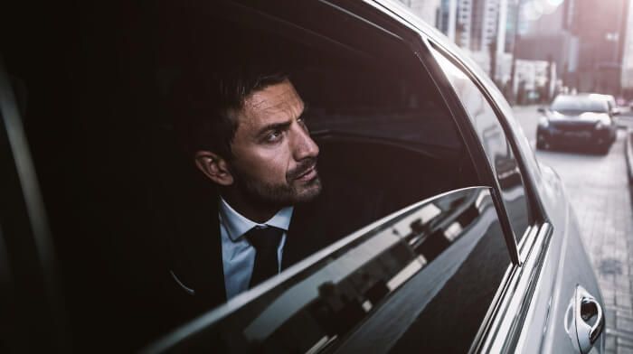 Man in a suit looking out a car window on a city street, with a serious expression.