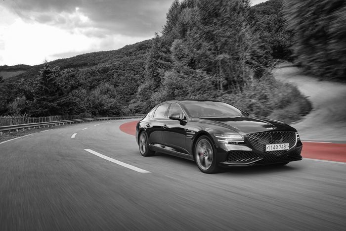Black sedan driving on a winding mountain road with red lane markings and a blurred grayscale landscape