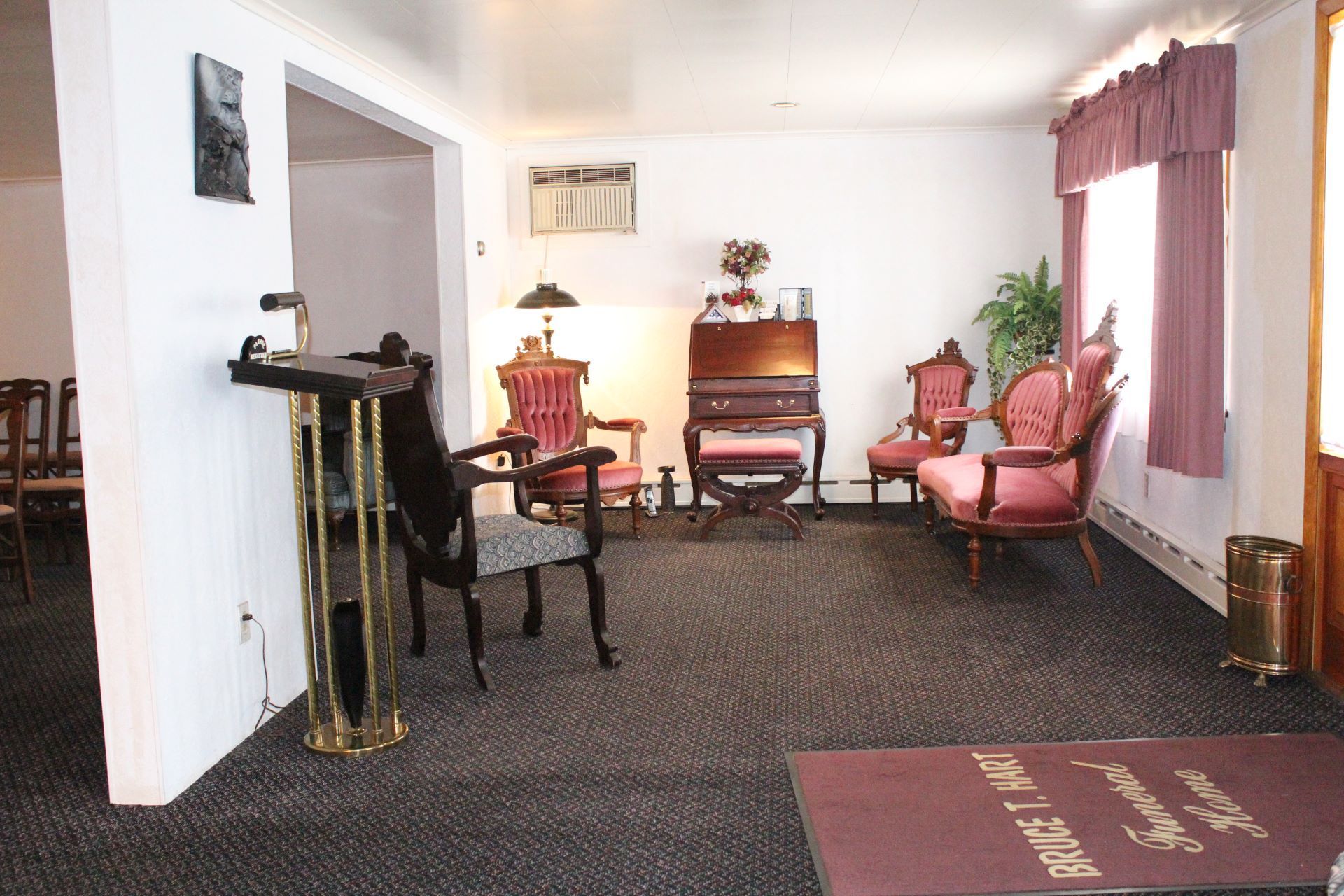 A living room with a piano and chairs and a red mat that says ' funeral home ' on it