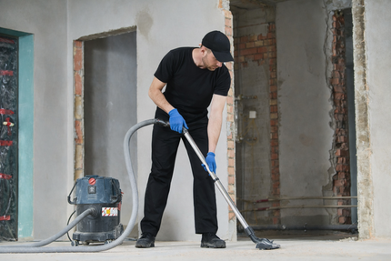 Man in black with gloves uses industrial vacuum at construction site with exposed brick walls