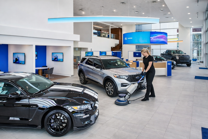 Person cleaning floor in modern car showroom beside black and silver vehicles with digital displays