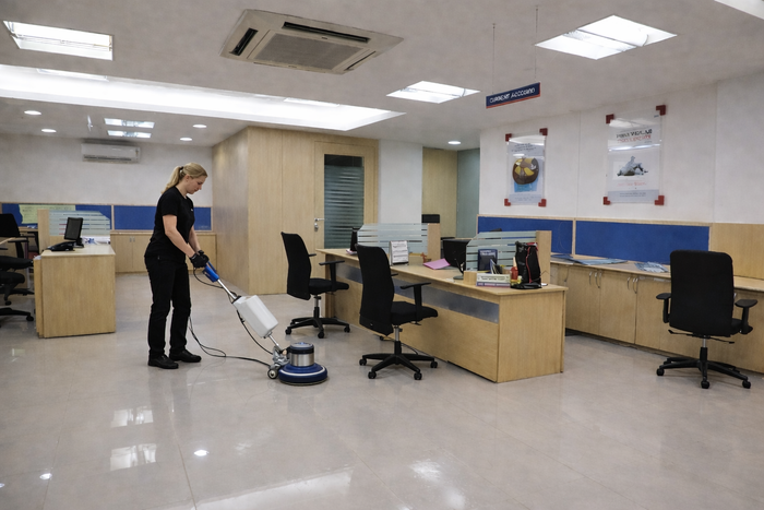 Woman operates floor cleaning machine in tidy, modern office with wooden desks and chairs
