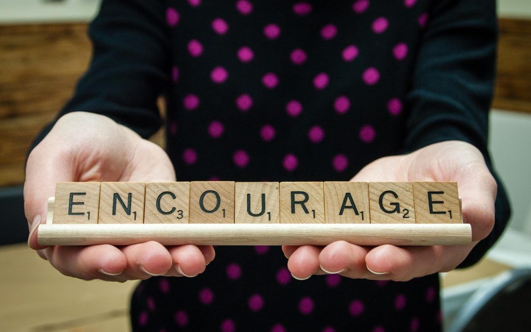 A person is holding scrabble tiles that spell out the word encourage.