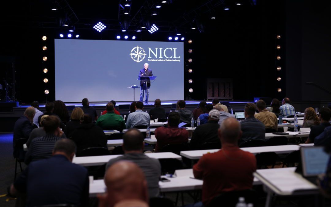 A man is giving a speech in front of a large screen that says nici.