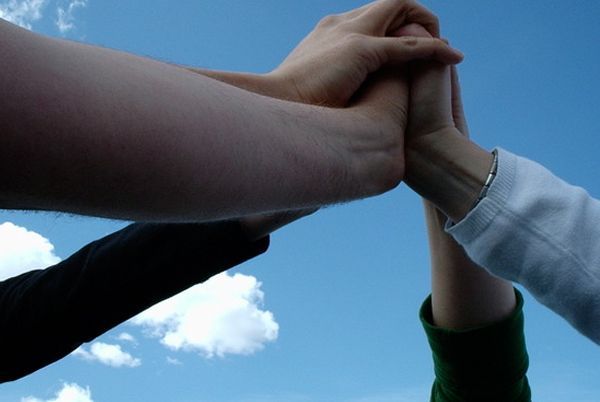 A group of people putting their hands together against a blue sky