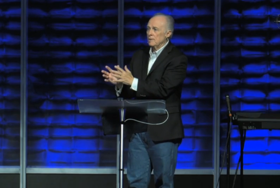 Dr. Mark Rutland  is standing at a podium with his hands folded