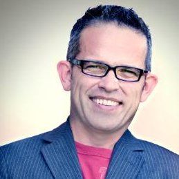 A man wearing glasses and a suit is smiling for the camera.